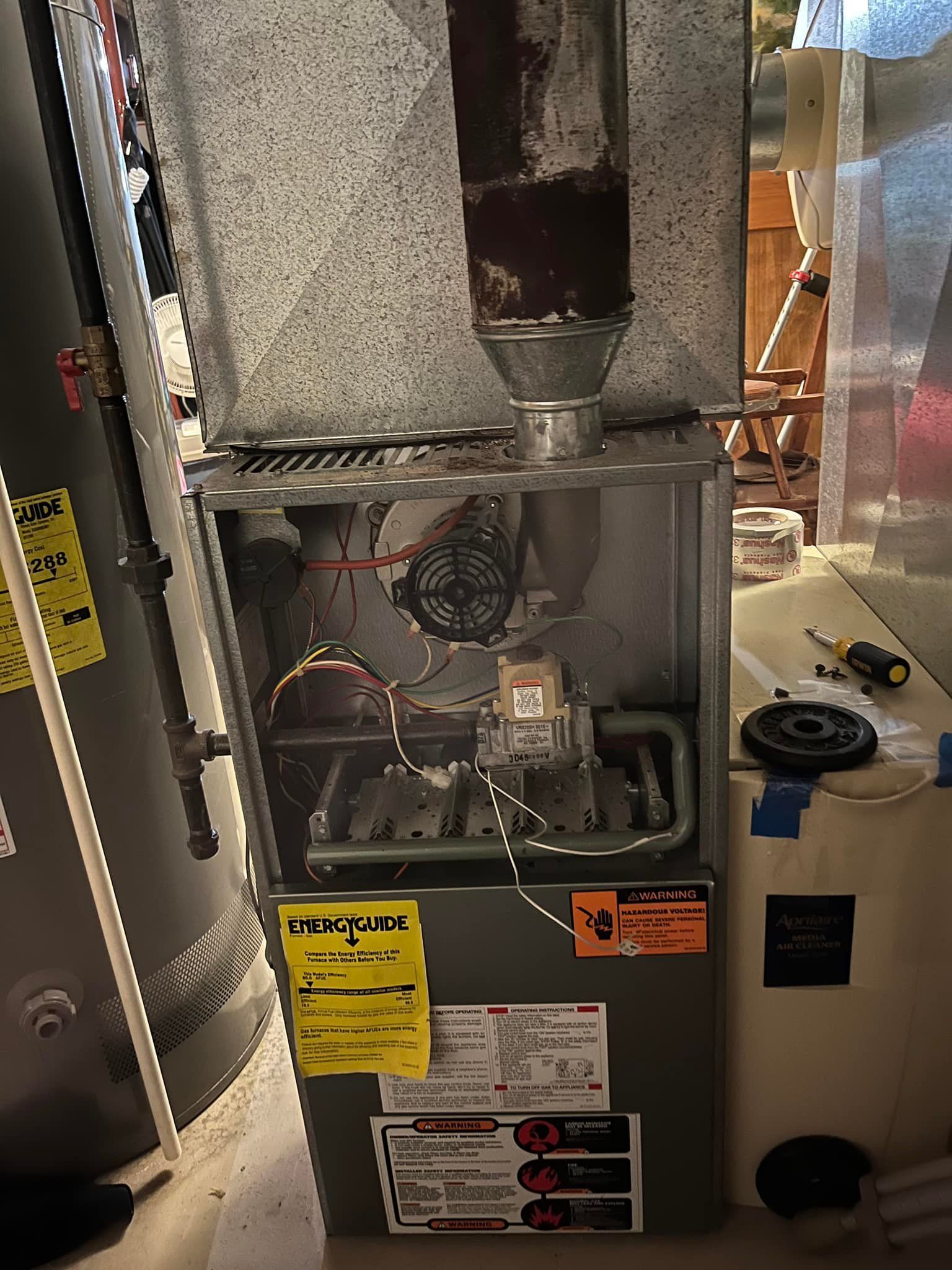 A furnace is sitting in a basement next to a water heater.