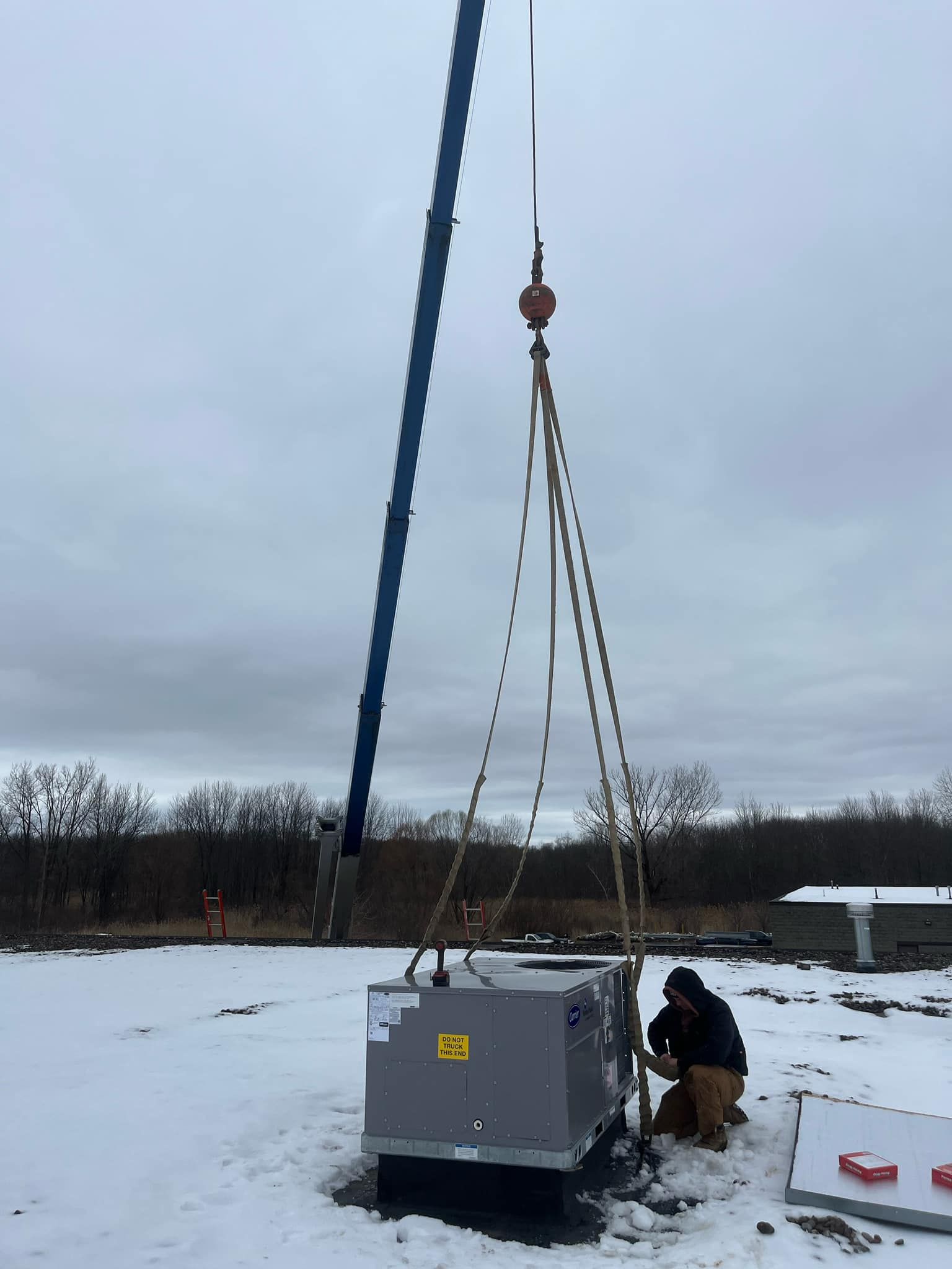 A man is working on an air conditioner in the snow with a crane.
