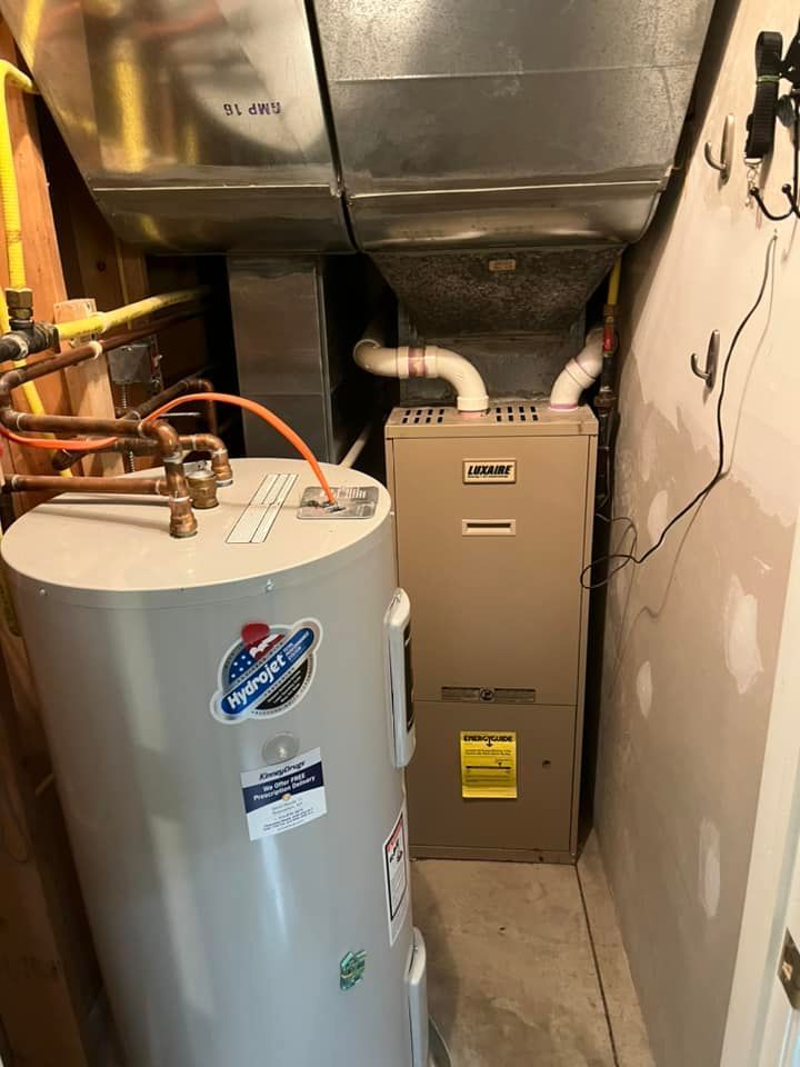 A water heater is sitting next to a furnace in a basement.
