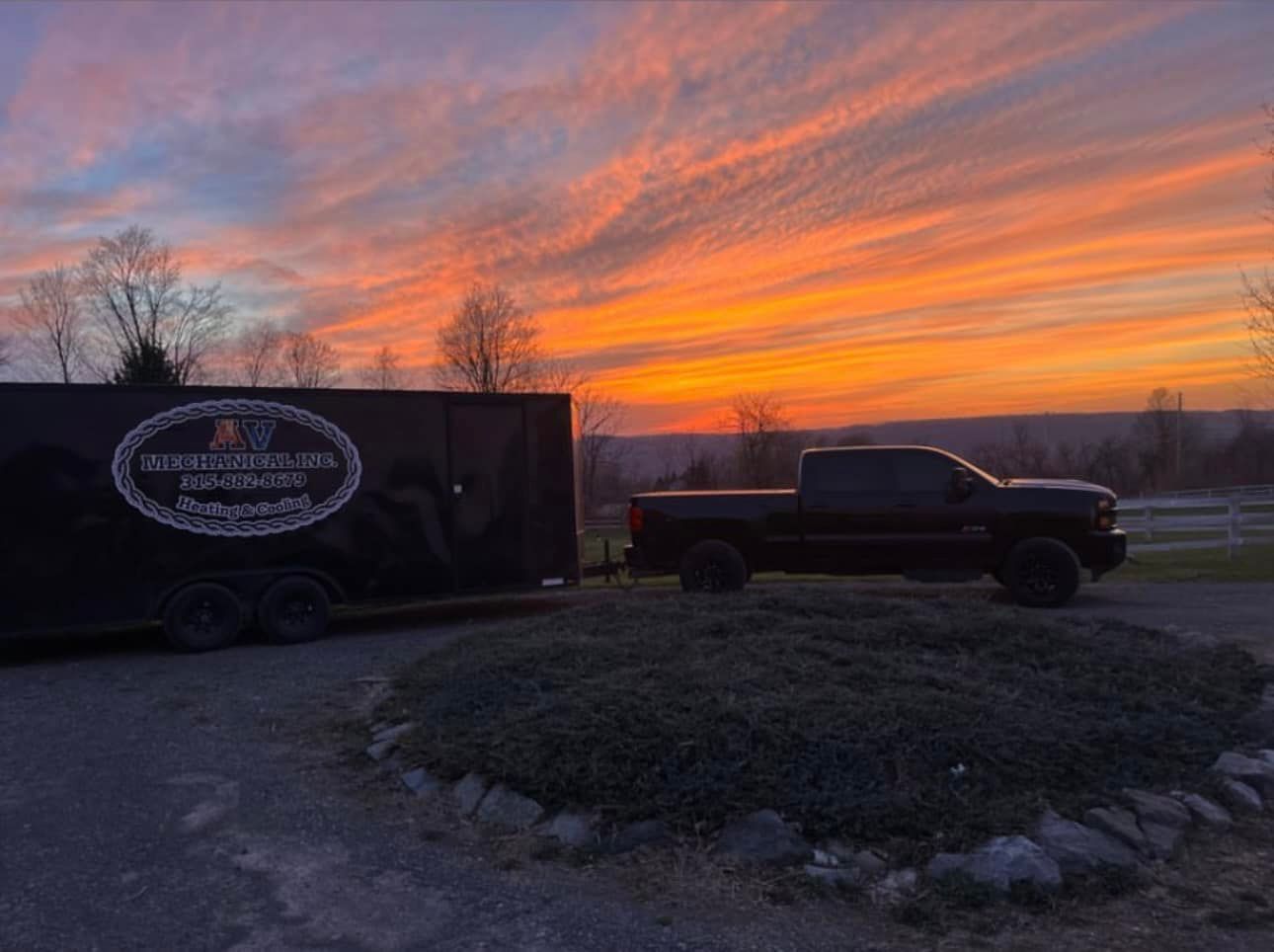 A truck and trailer are parked in front of a sunset.