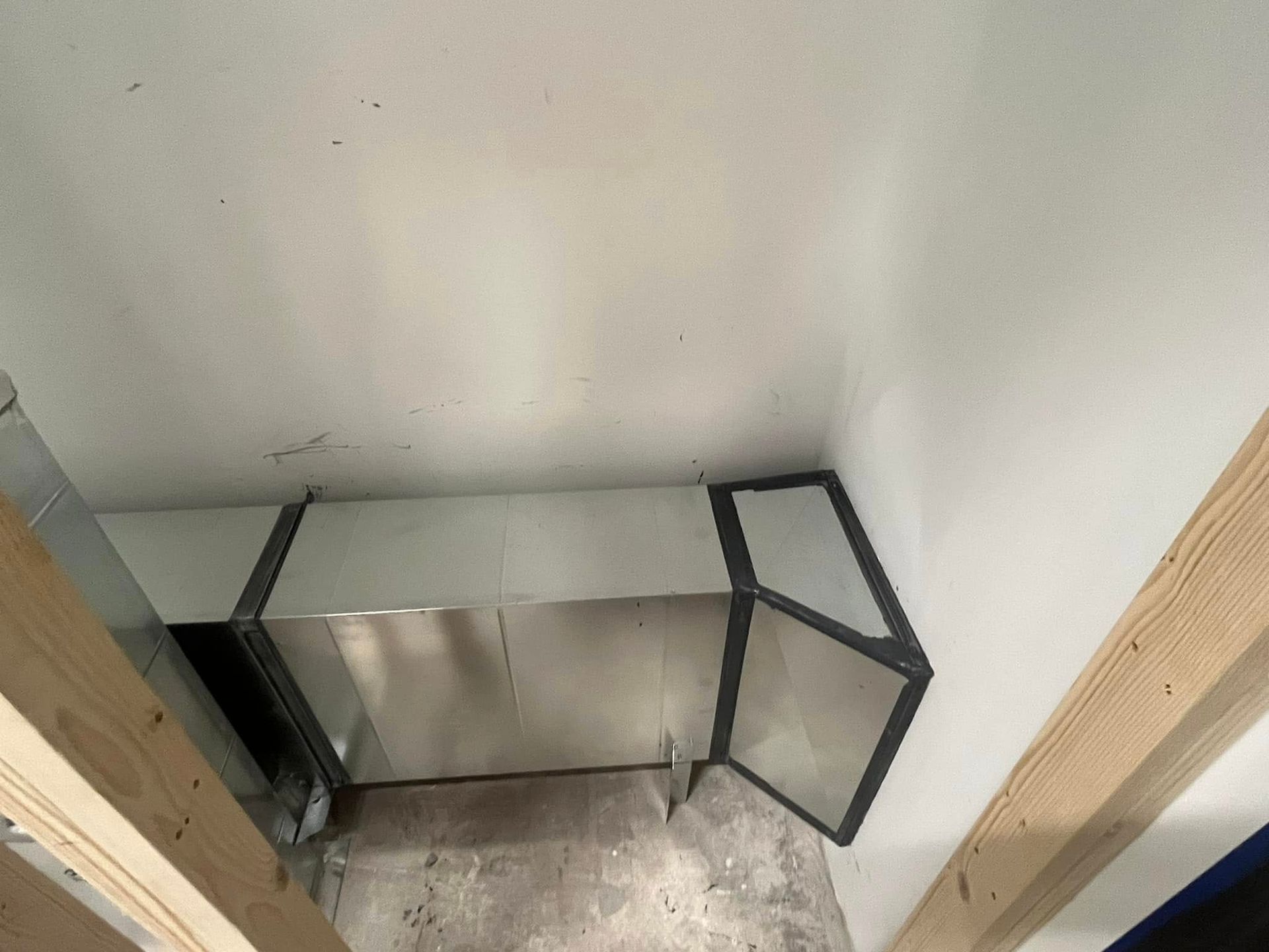 A corner of a room with a stainless steel pipe coming out of it.