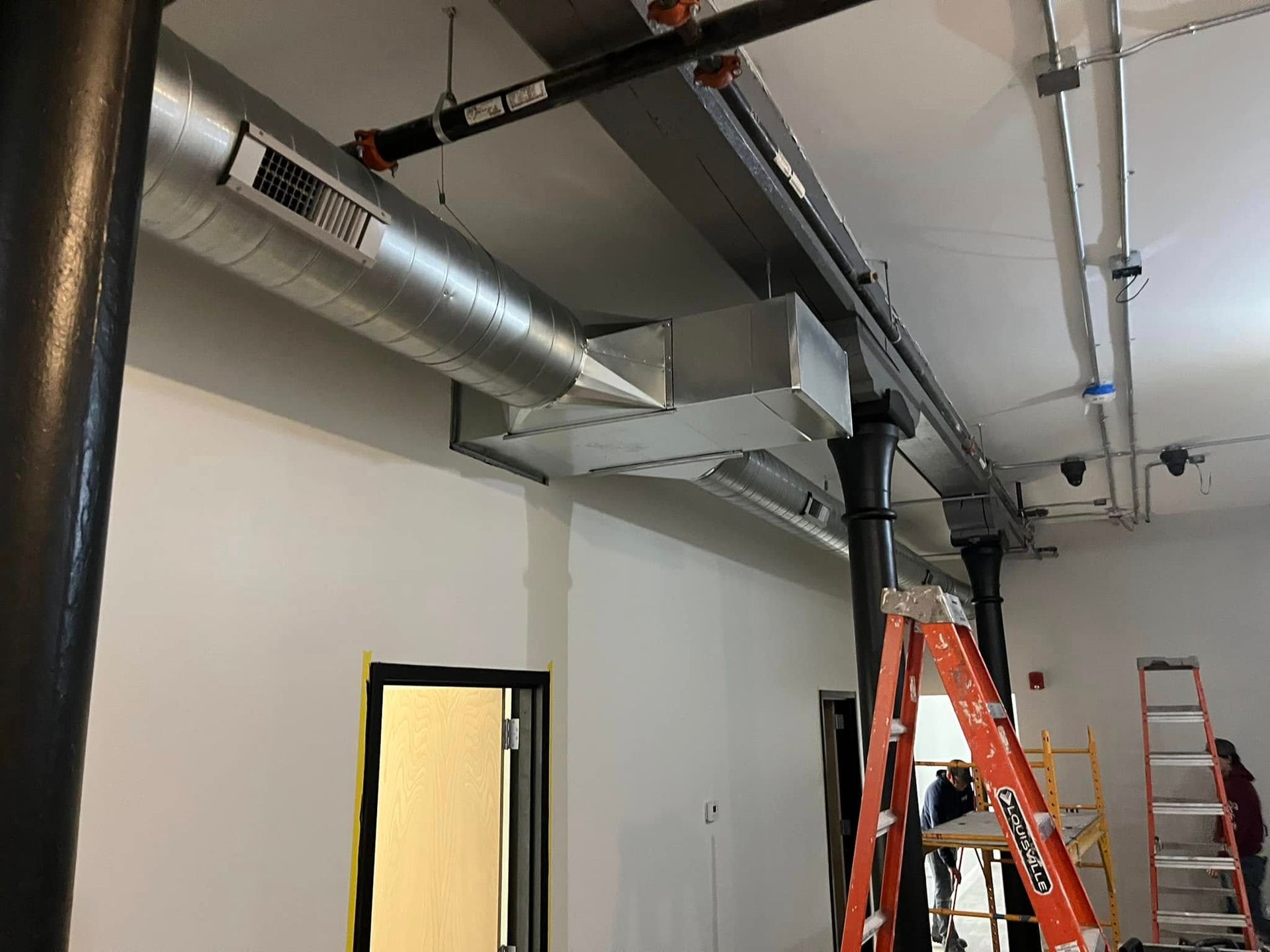A room with a ladder and pipes hanging from the ceiling