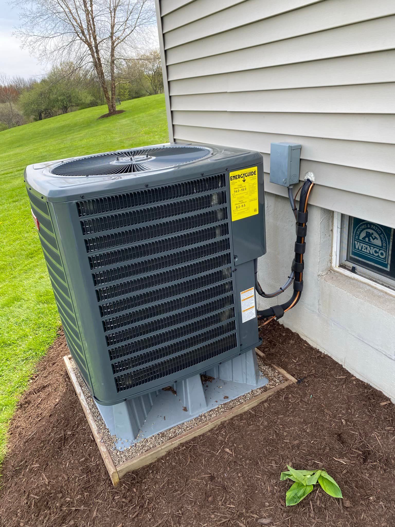 An air conditioner is sitting on the side of a house next to a window.