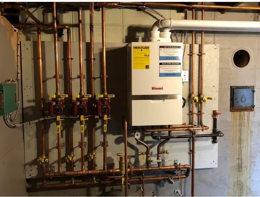 A white boiler is sitting on a wall surrounded by copper pipes.