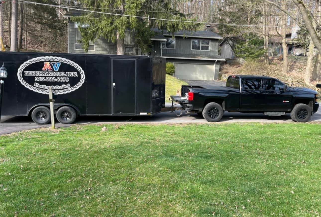 A black truck is towing a black trailer in a driveway.
