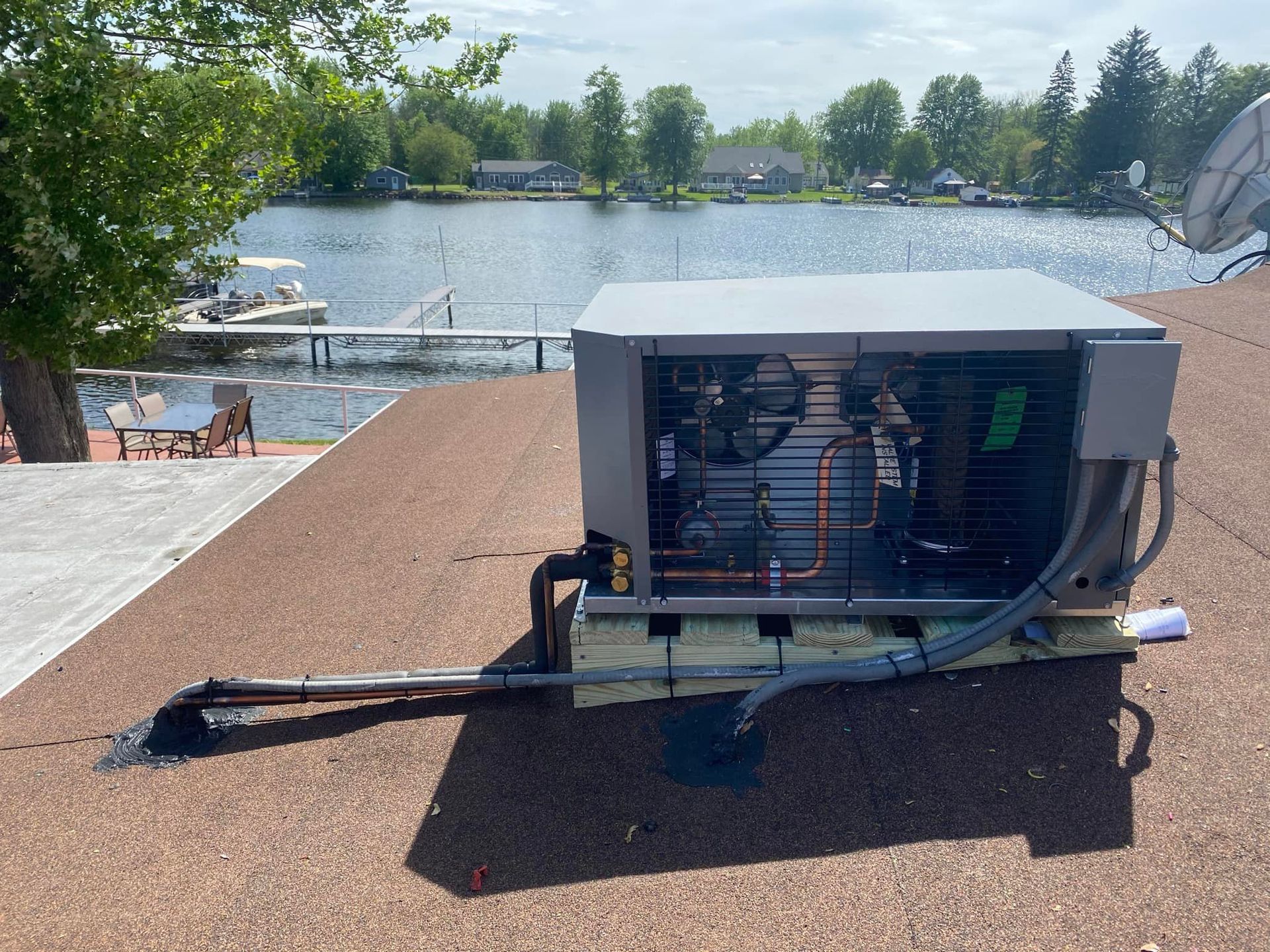 A large air conditioner is sitting on top of a roof next to a lake.