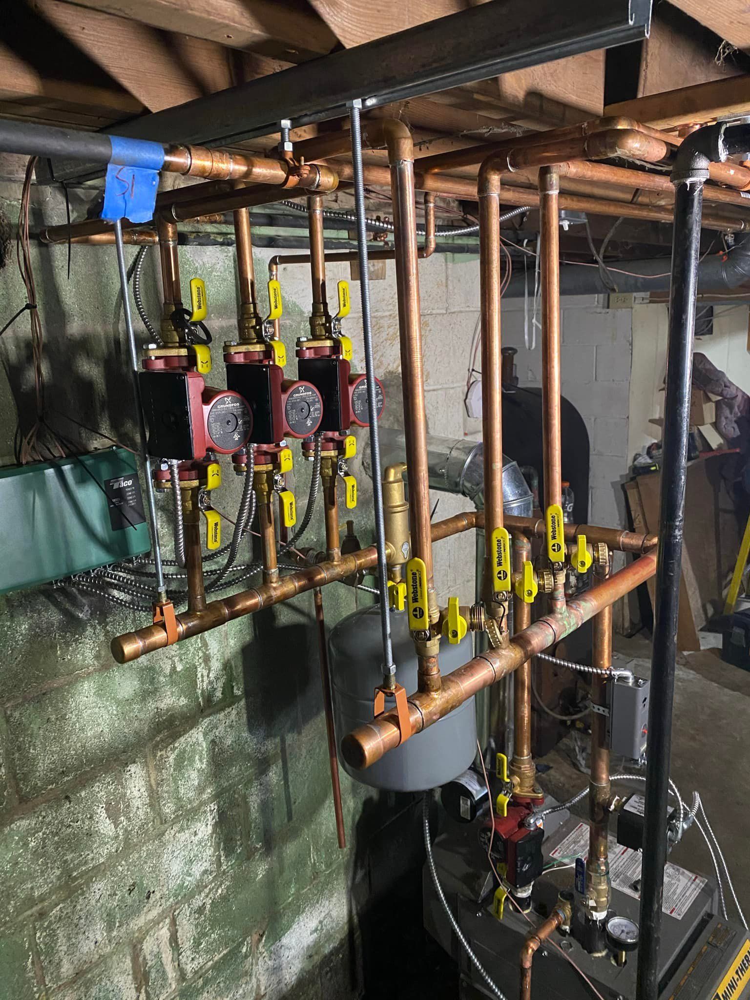 A bunch of copper pipes are hanging from the ceiling in a basement.