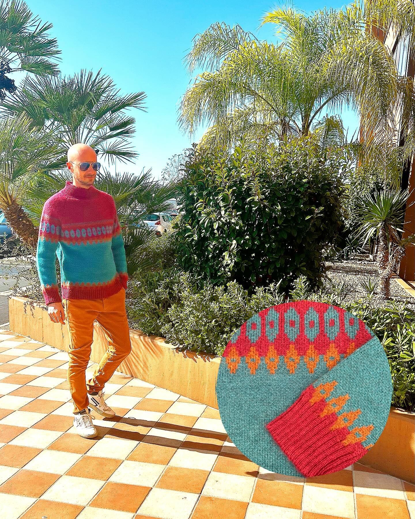 Un uomo che indossa un maglione colorato è in piedi su un pavimento a scacchi.