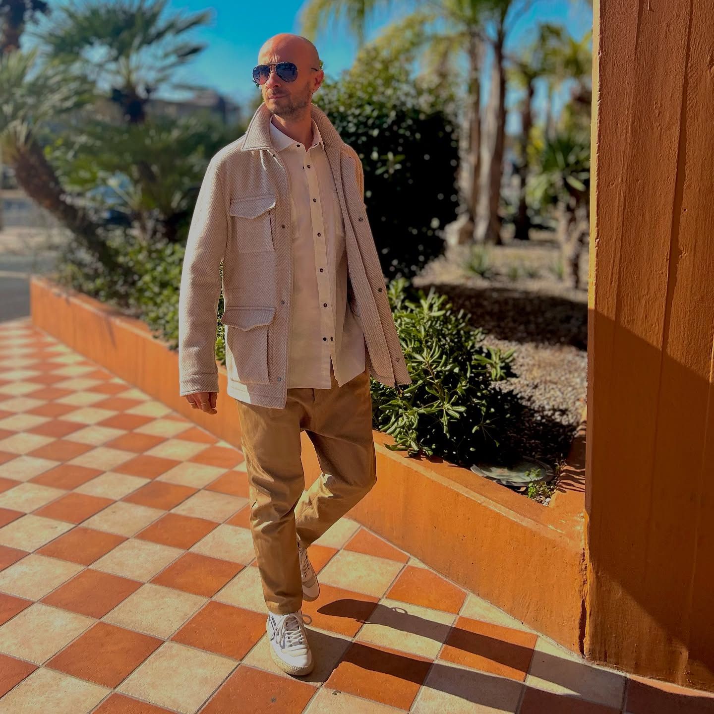 Un uomo che indossa occhiali da sole e una giacca bianca è in piedi su un pavimento a scacchi