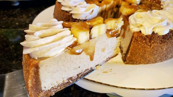 A slice of cheesecake is being taken out of a cheesecake on a plate.