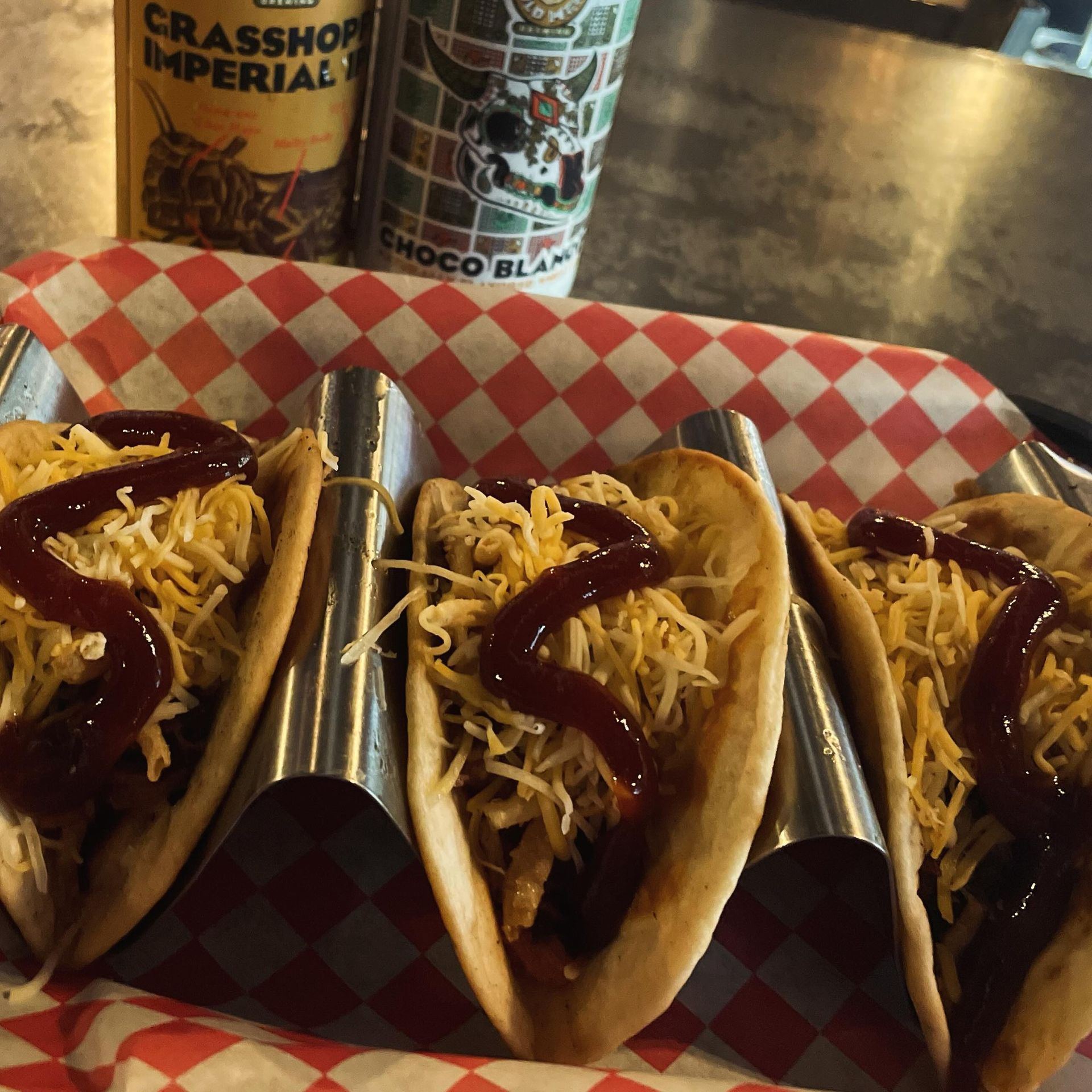 A tray of tacos with ketchup and cheese next to a can of grasshopper imperial