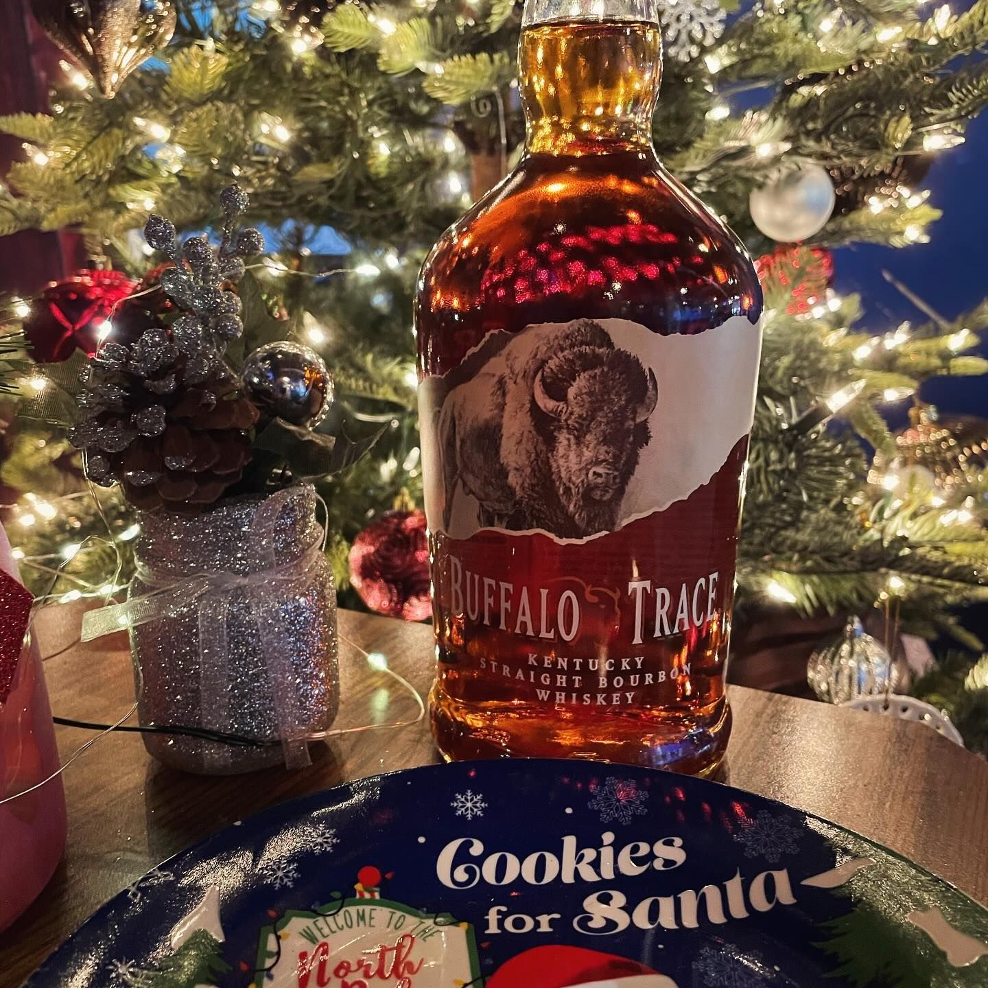 A bottle of buffalo trace whiskey is sitting on a table next to a christmas tree.