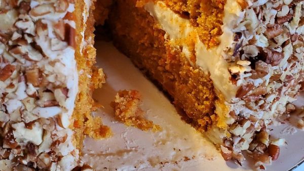A close up of a carrot cake with a slice taken out of it on a plate.