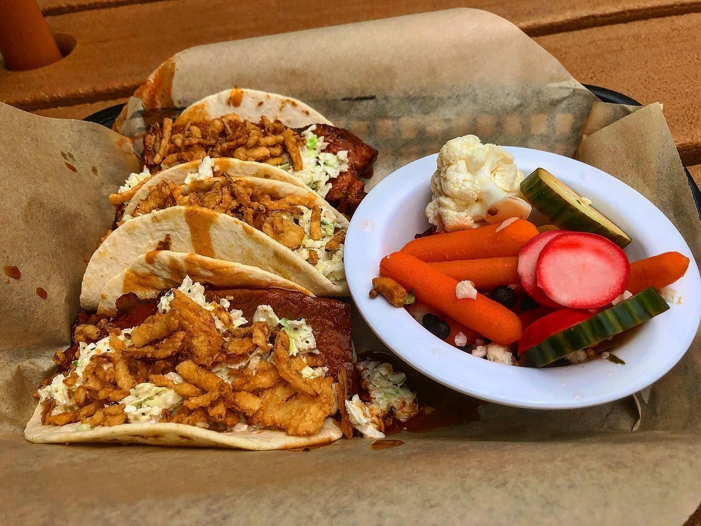 A basket of tacos and a bowl of vegetables on a table.