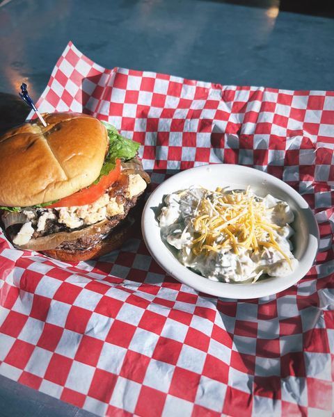 A hamburger and a bowl of potato salad on checkered paper