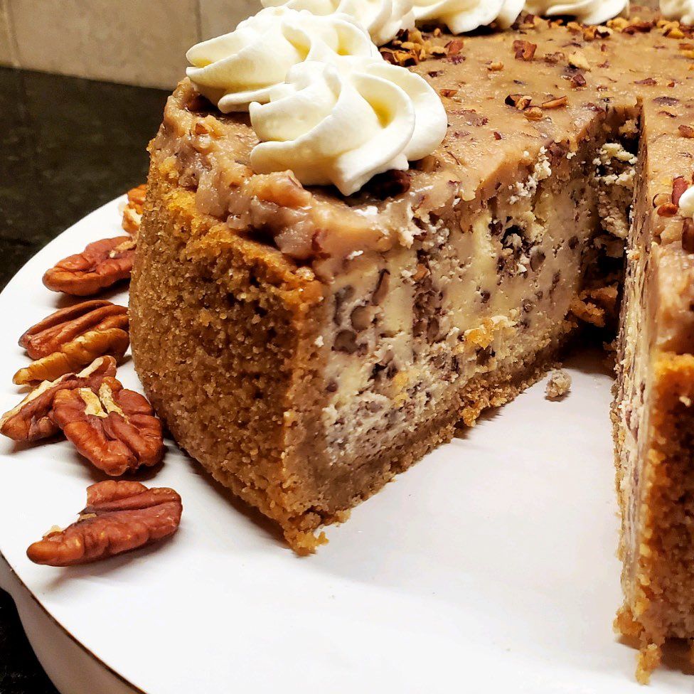 A pecan cheesecake with whipped cream and pecans on a white plate