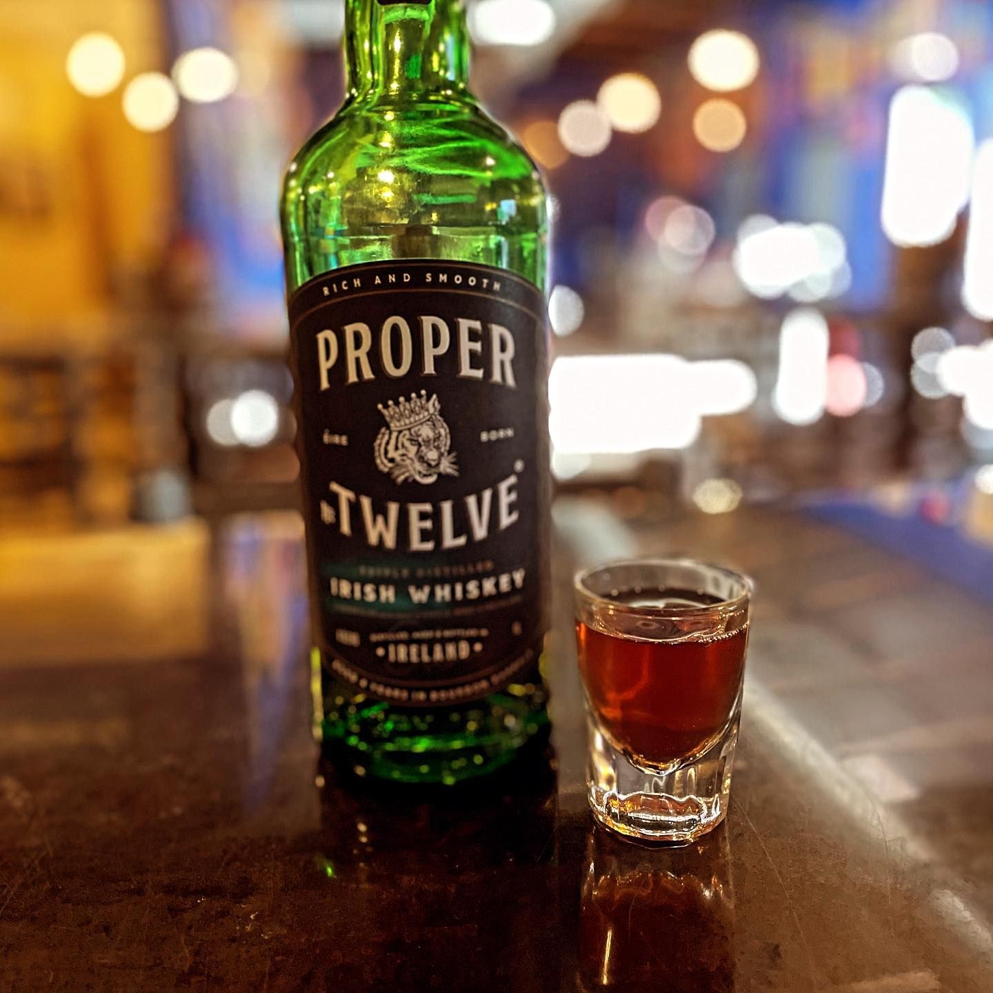 A bottle of proper twelve irish whiskey next to a shot glass
