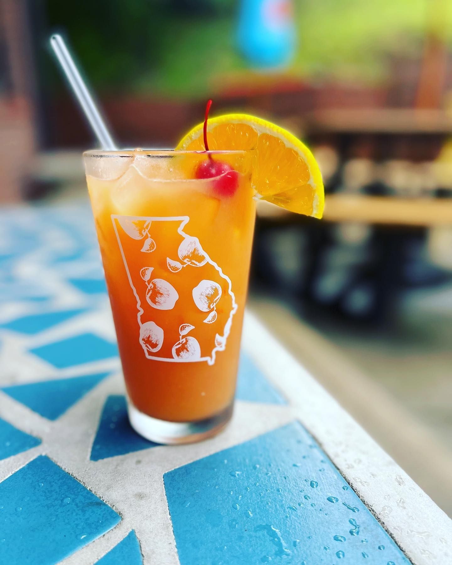 A glass of orange juice with a straw and a cherry on top