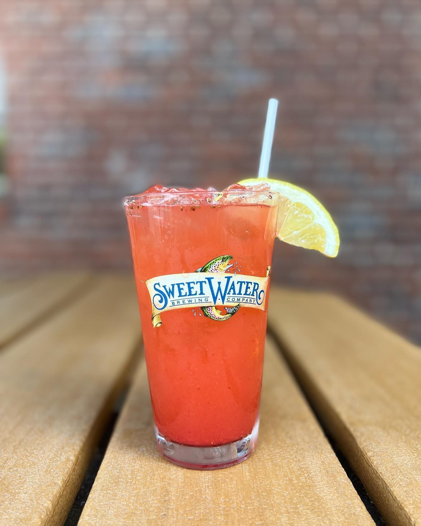 A glass of strawberry lemonade with a straw on a wooden table.