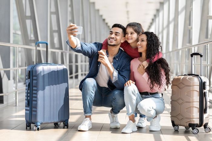 A family is taking a selfie at the airport with their luggage.