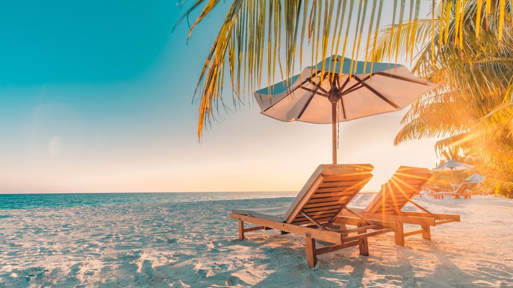 There are two chairs and an umbrella on the beach.