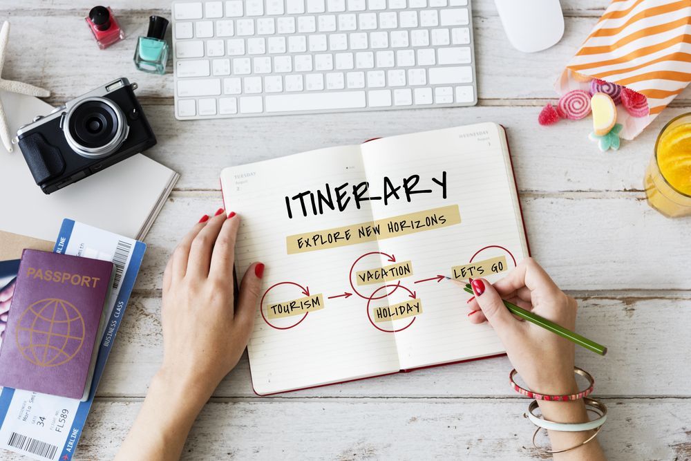 A person is writing in a notebook with the word itinerary on it.