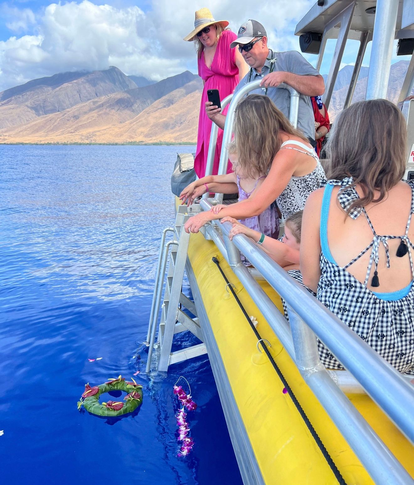 People on a boat near mountains release leis into the ocean.