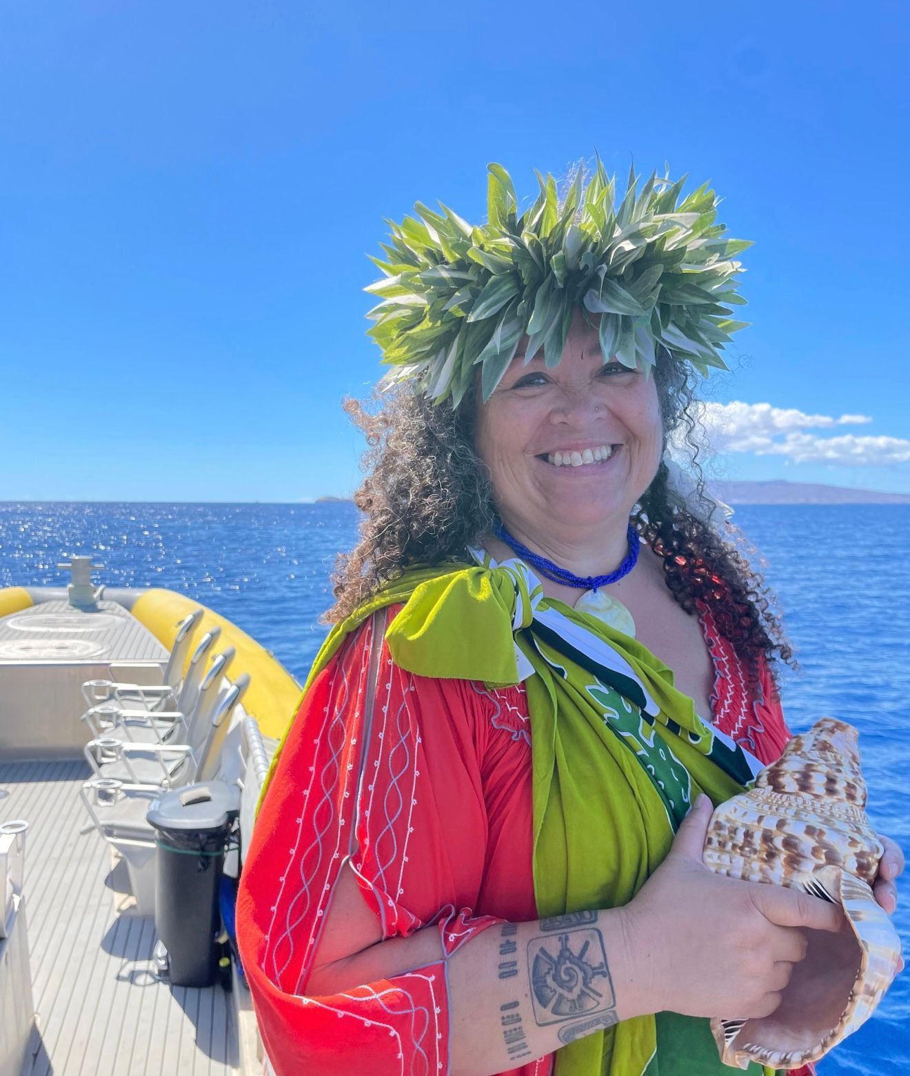 Woman on a boat, wearing lei and holding seashell, smiling at the camera, ocean background.