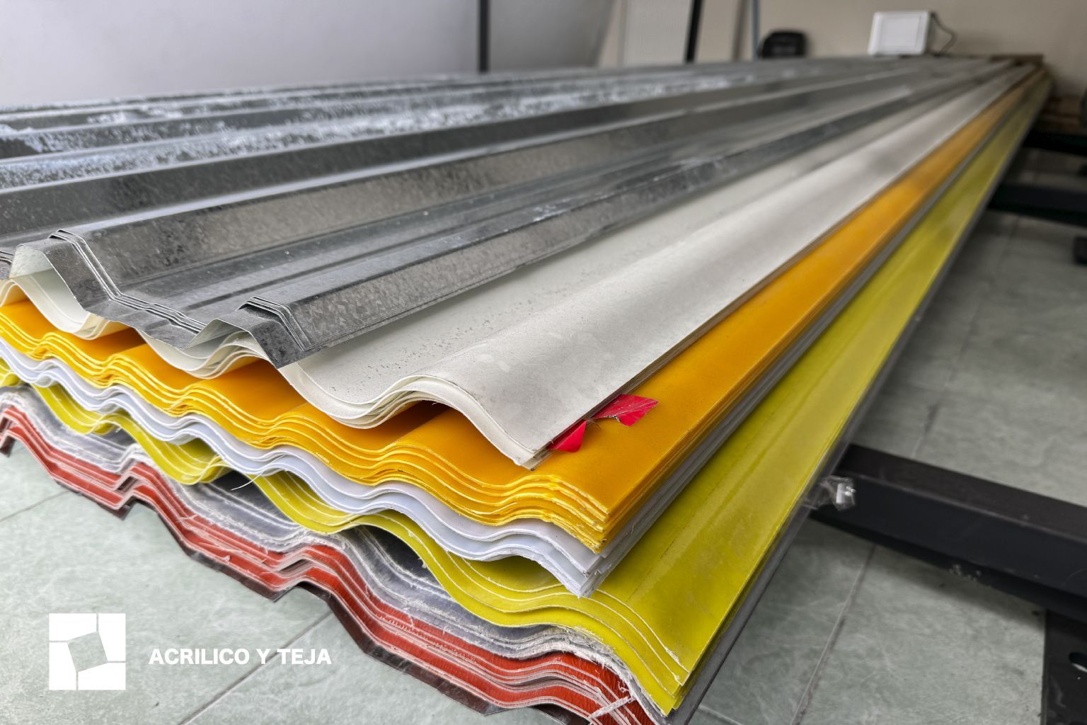 Una pila de láminas de techo onduladas en tonos amarillos, blancos y gris metalizado en un almacén interior.