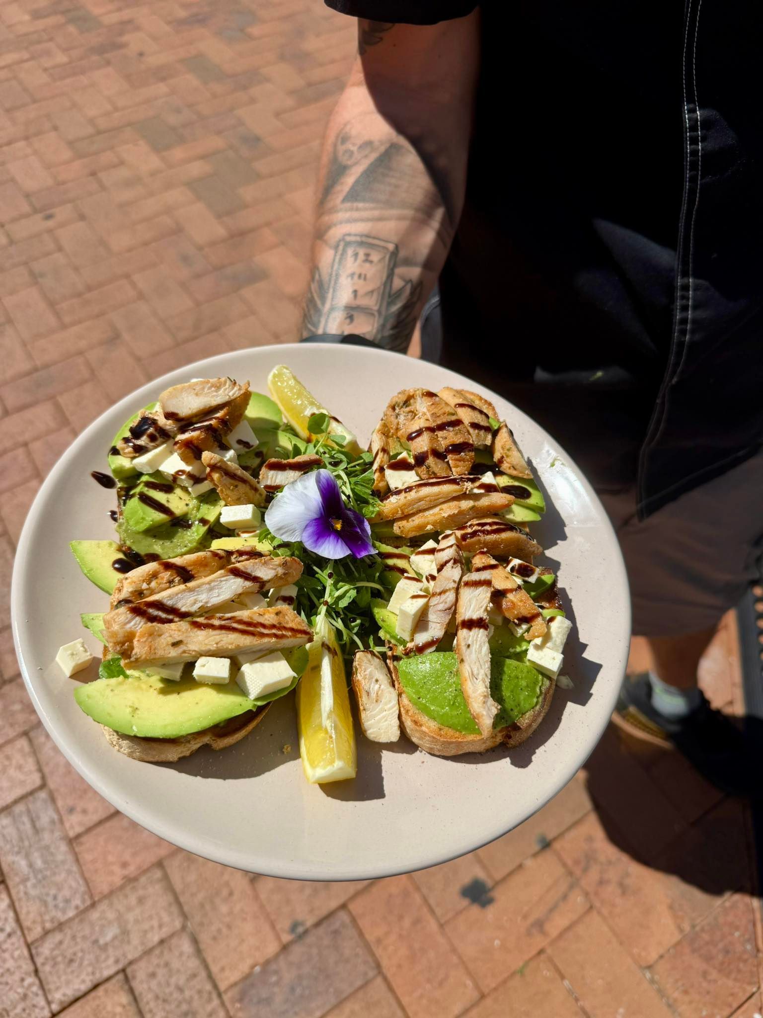 Plate of avocado toast with chicken and garnish held by person outdoors.— Relax in Paradise in Yeppoon, QLD