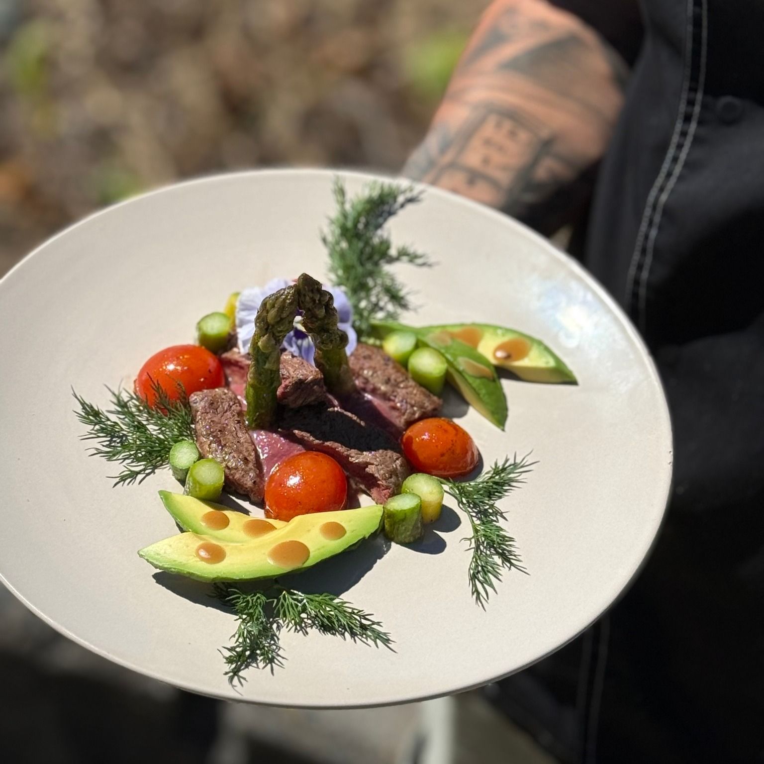 Plate of food: steak, tomatoes, asparagus, avocado, dill, with sauce. Held by person.— Relax in Paradise in Yeppoon, QLD