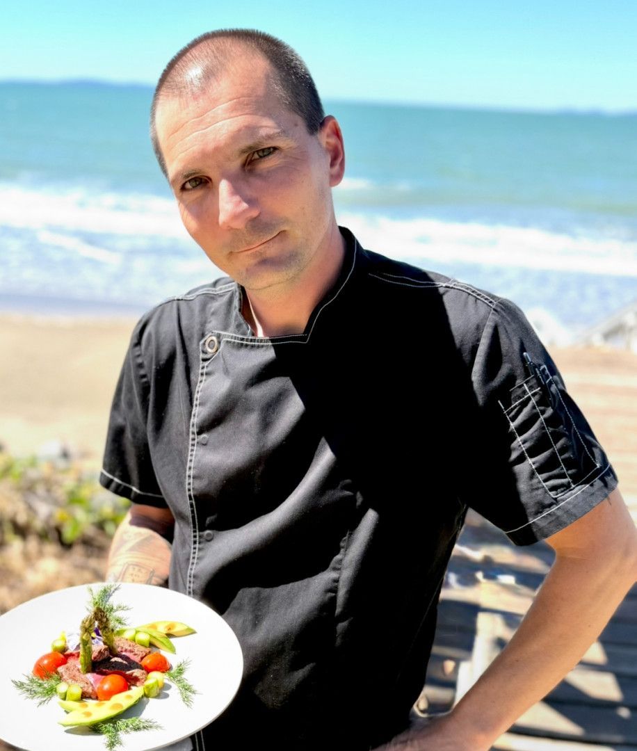Chef holding plate with food, beach background.— Relax in Paradise in Yeppoon, QLD