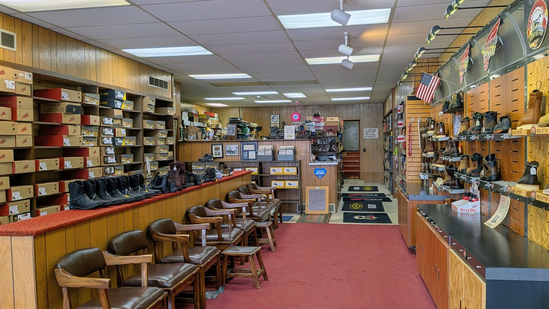 Narrow shop interior with shelves of shoes, stools, display cases, and red carpet aisle