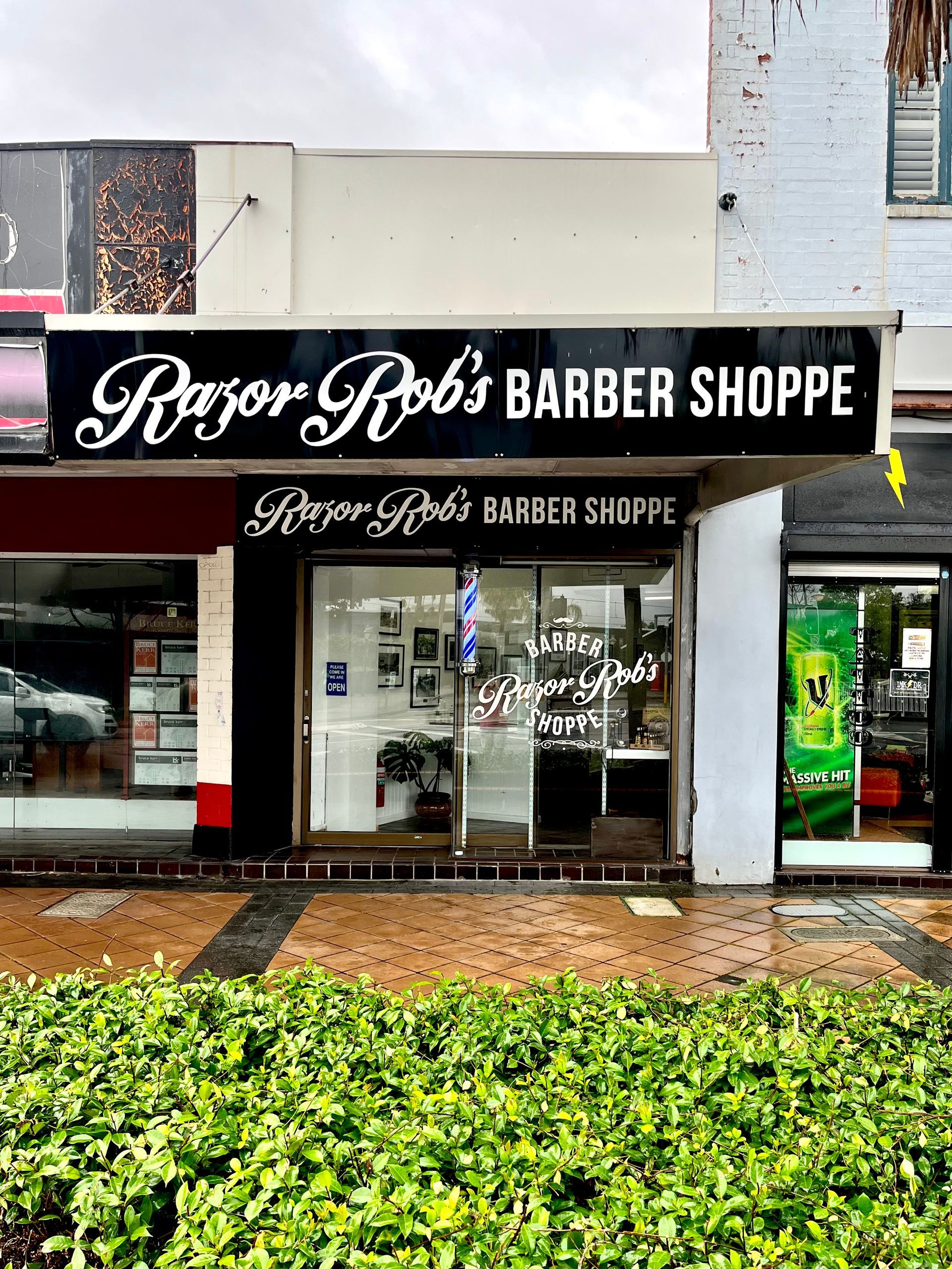 Exterior of Razor Rob's Barber Shoppe, with a lit black sign and a storefront entrance.