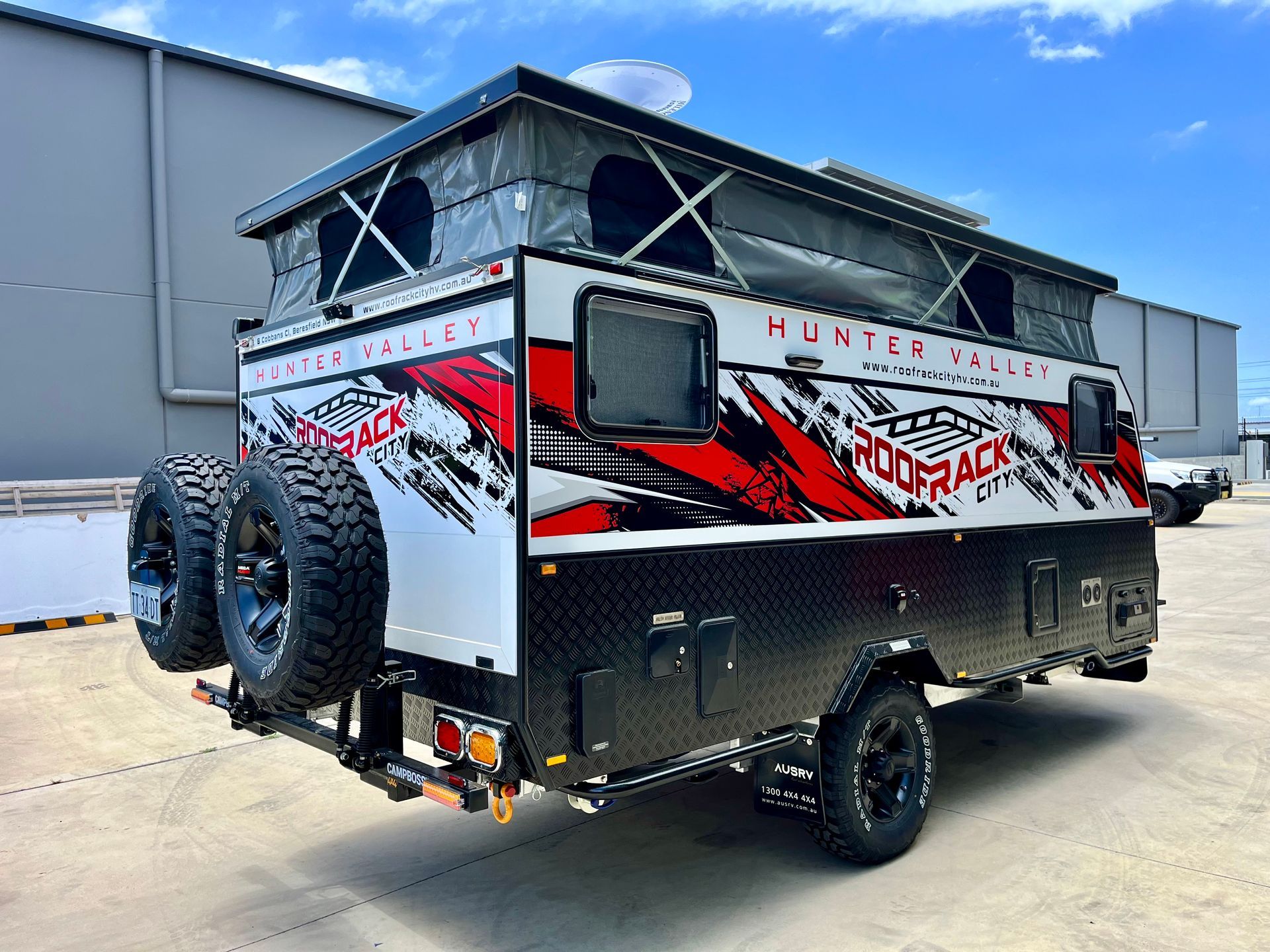 White and black off-road camper trailer with red accents, spare tires, and pop-up roof. 