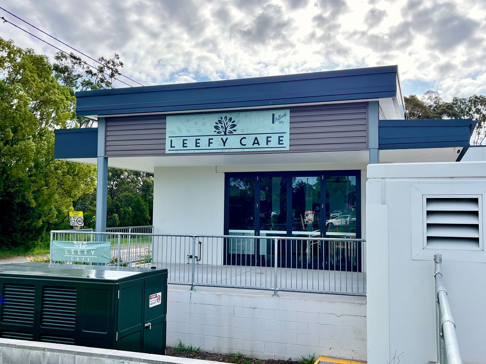 Leefy Cafe exterior, white building with gray accents, glass door, sign above, metal railing.