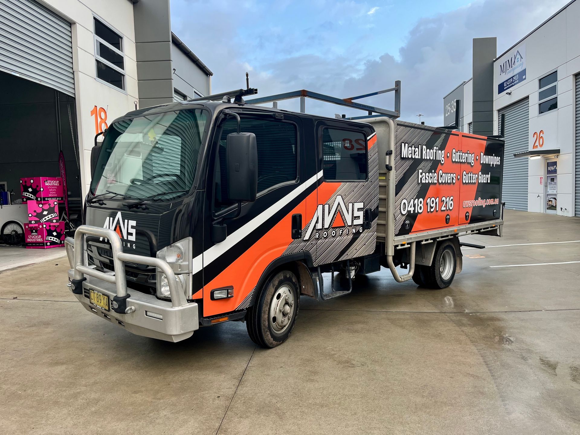 Black and orange work truck with ladder rack parked outside a warehouse.