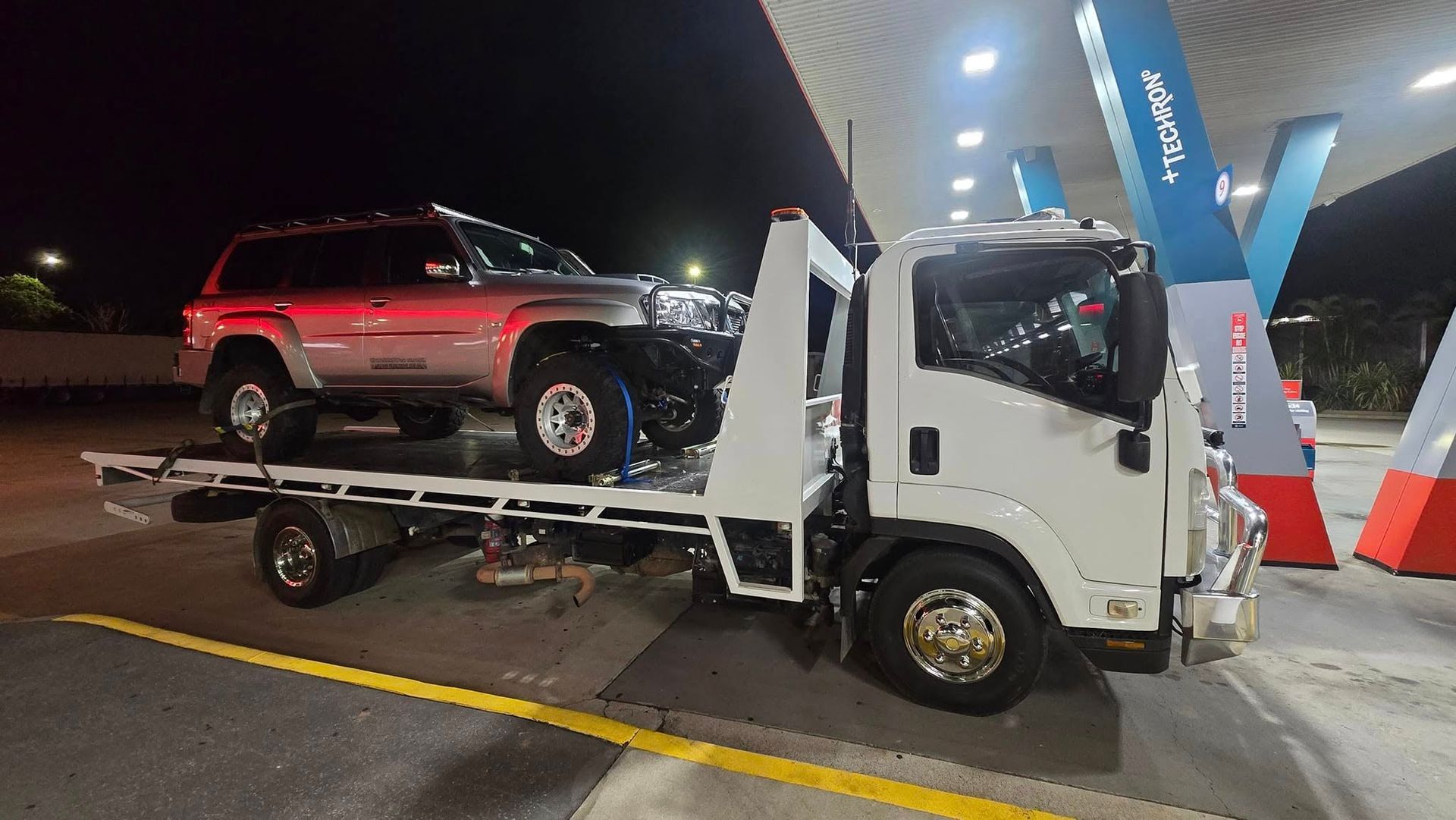 Tow Truck Carrying a Silver Suv at a Gas Station at Night — GTS - Gardiner Transport Solutions in Berserker, QLD