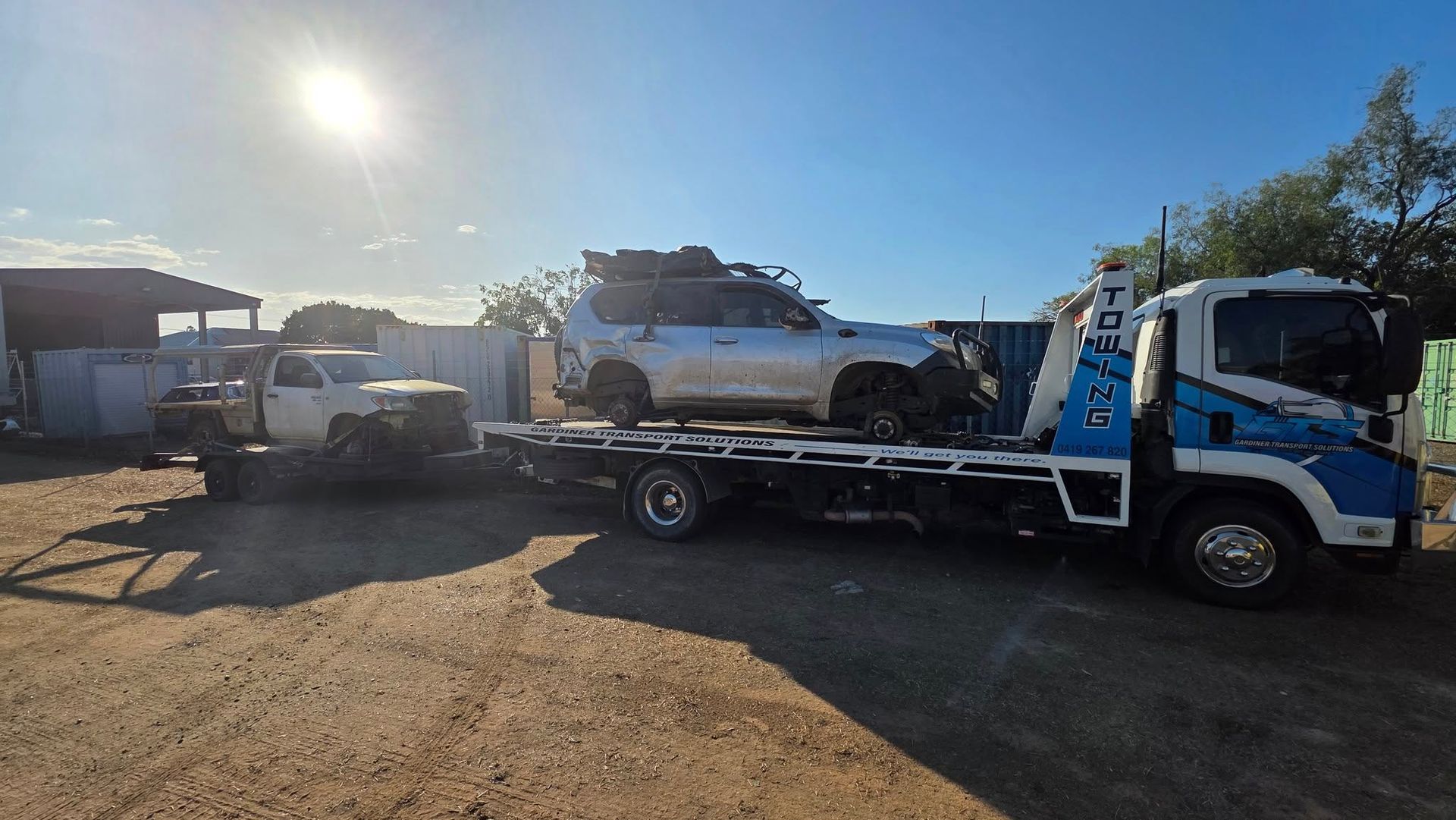 Tow Truck Carrying Two Damaged White Vehicles Under a Bright Sun — GTS - Gardiner Transport Solutions in Berserker, QLD