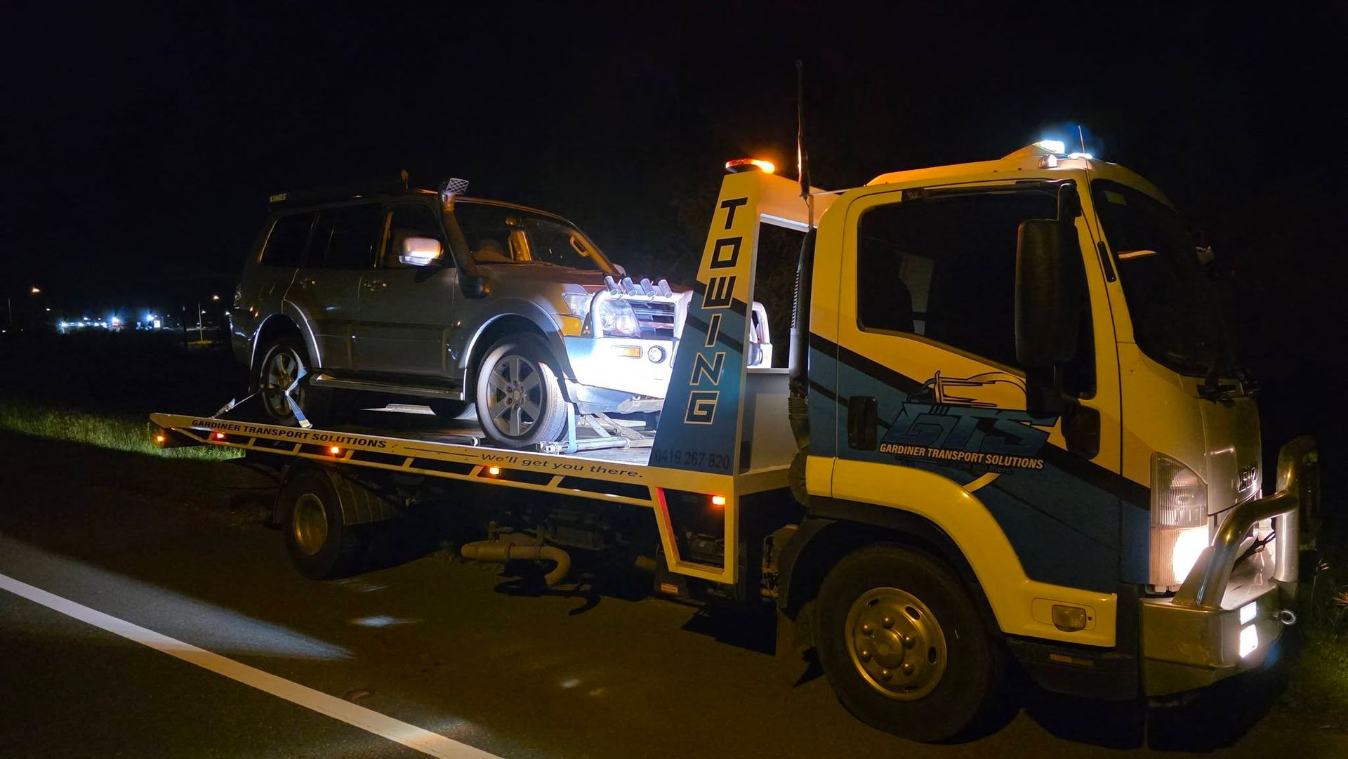 Tow truck at night, towing a gray SUV. Headlights on, roadside setting — GTS - Gardiner Transport Solutions in Berserker, QLD