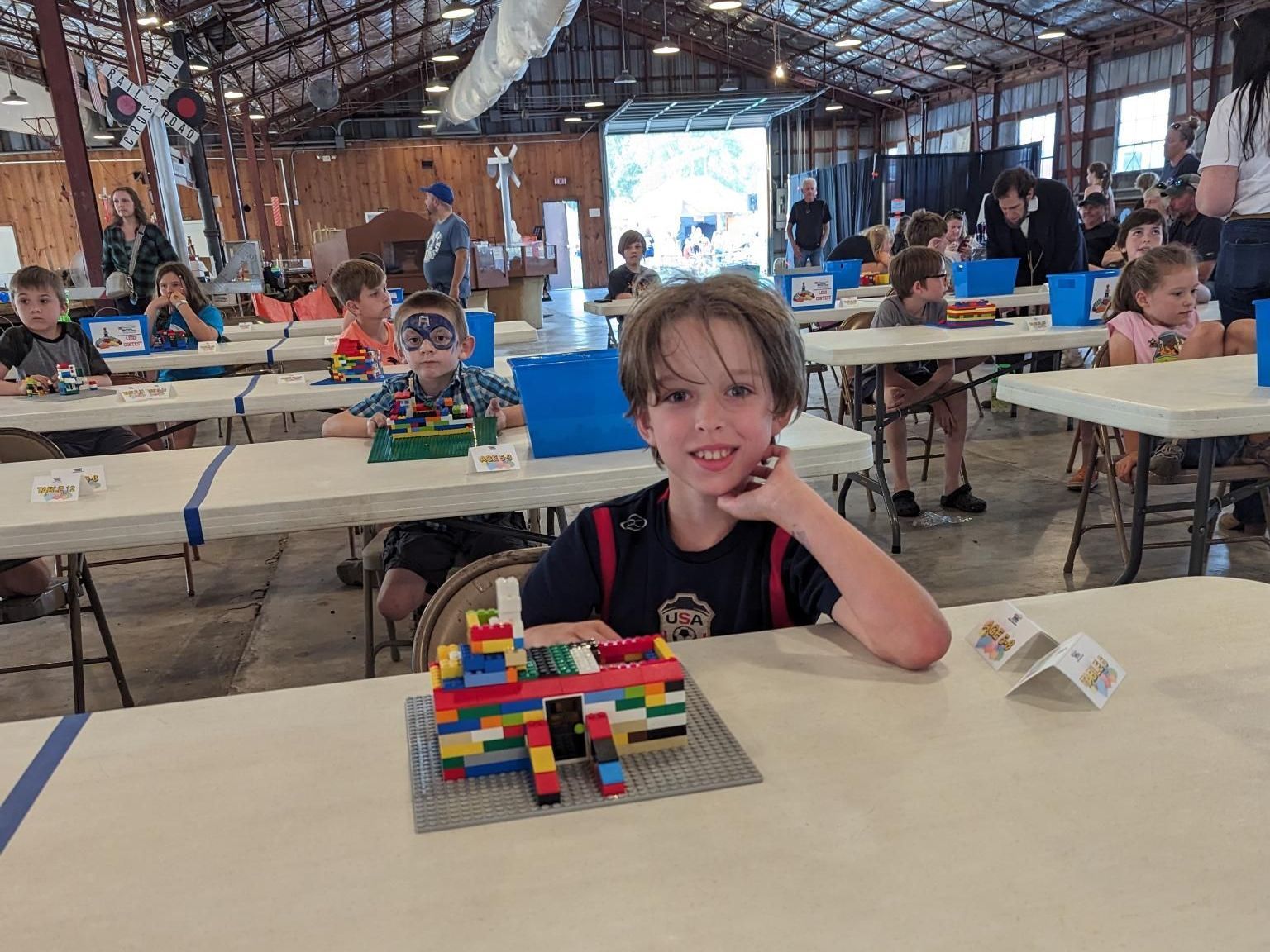 A boy is sitting at a table with a lego model on it.