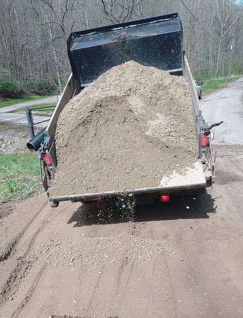 A dump truck is carrying a large pile of dirt on a dirt road.