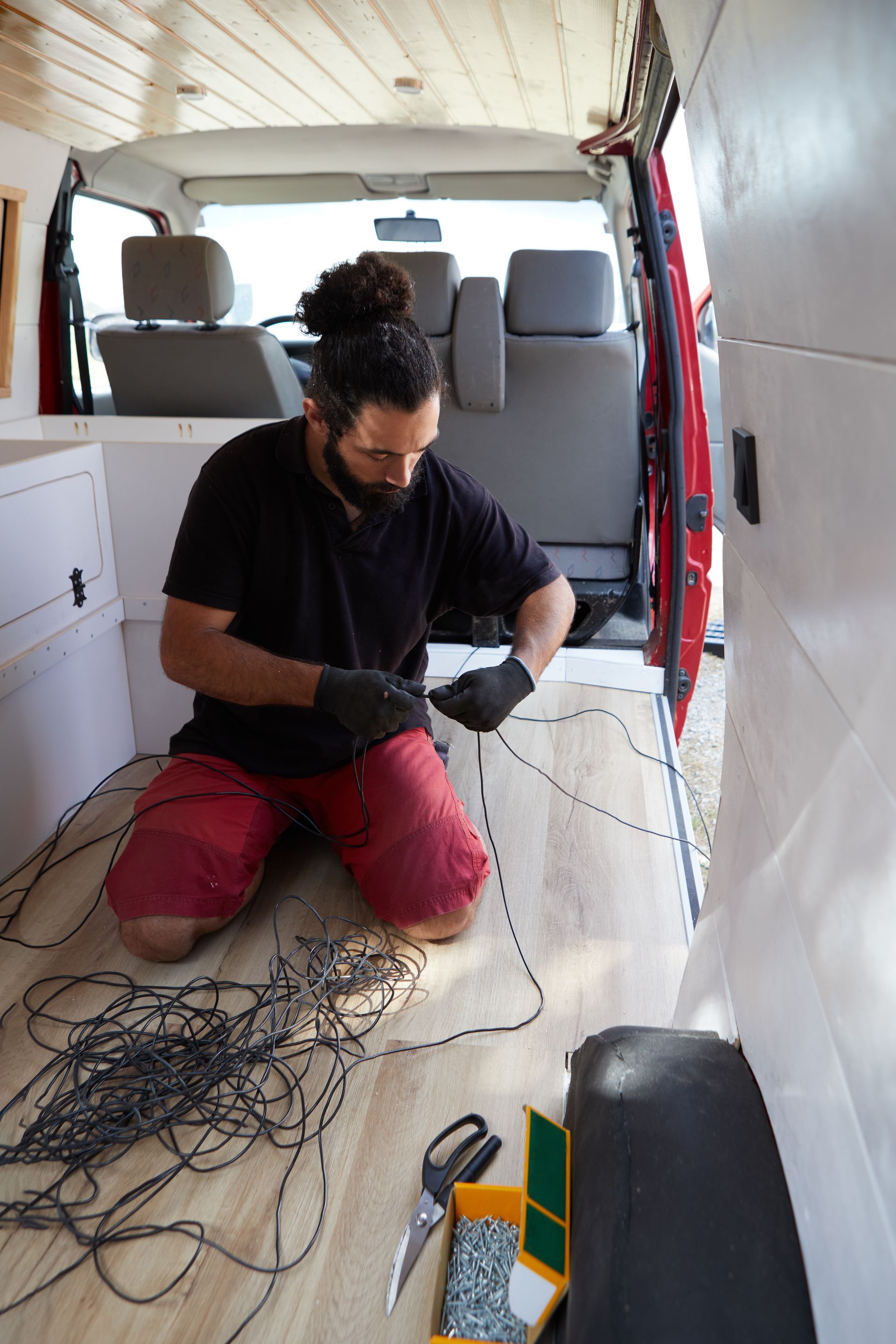A man works on a van in the middle of an RV repair shop, surrounded by tools and equipment. A man works on a van in the middle of an RV repair shop, surrounded by tools and equipment.