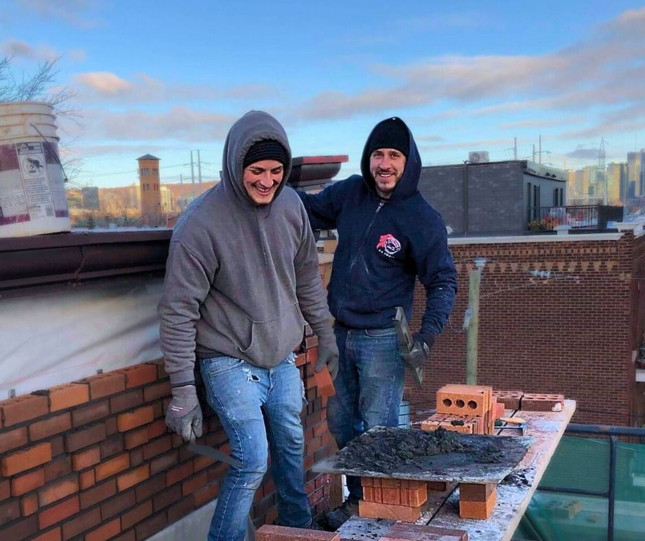 Deux hommes travaillent sur un mur de briques au sommet d'un bâtiment.