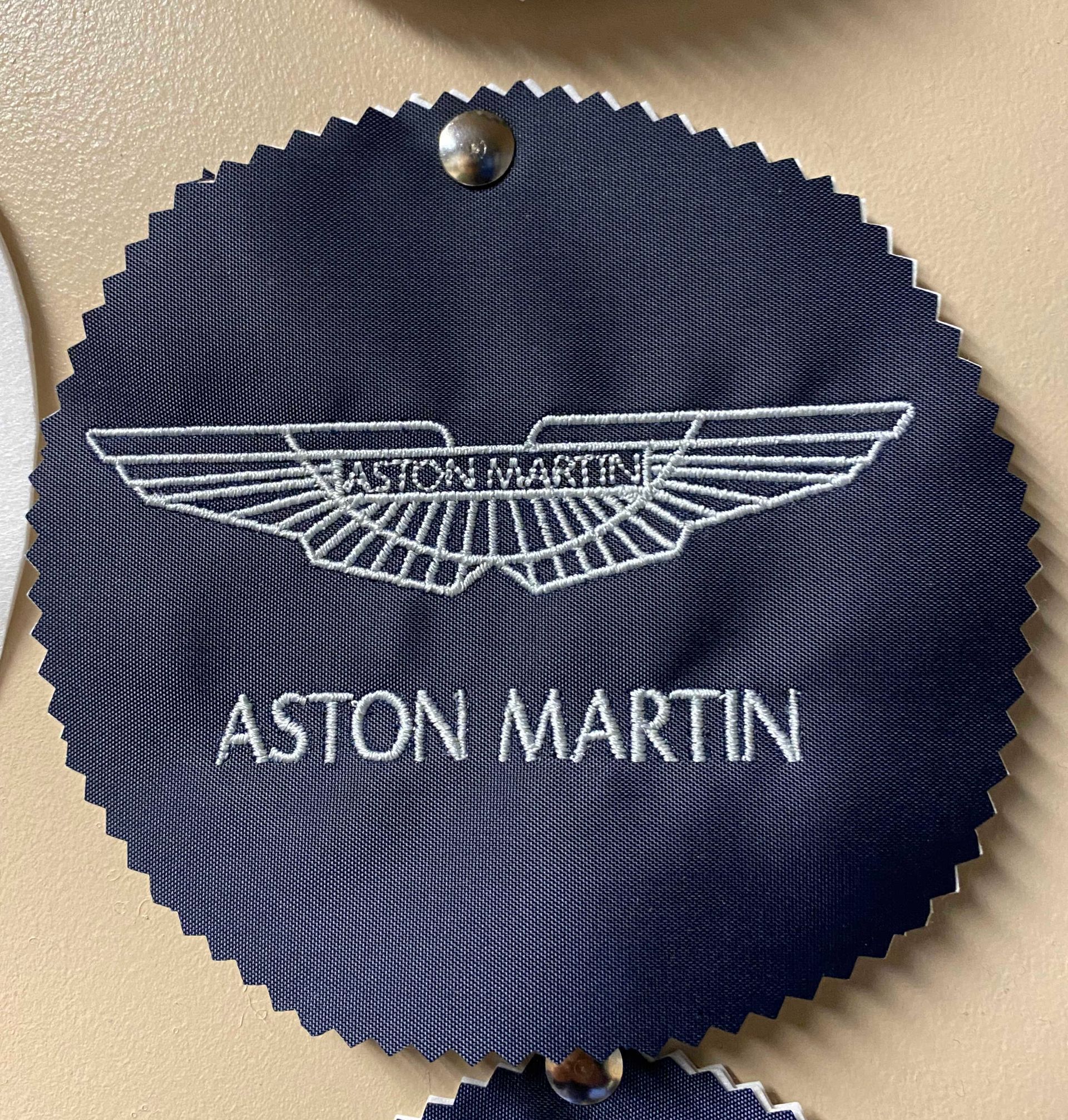 A dark blue Aston Martin fabric swatch with the brand's logo embroidered in white.