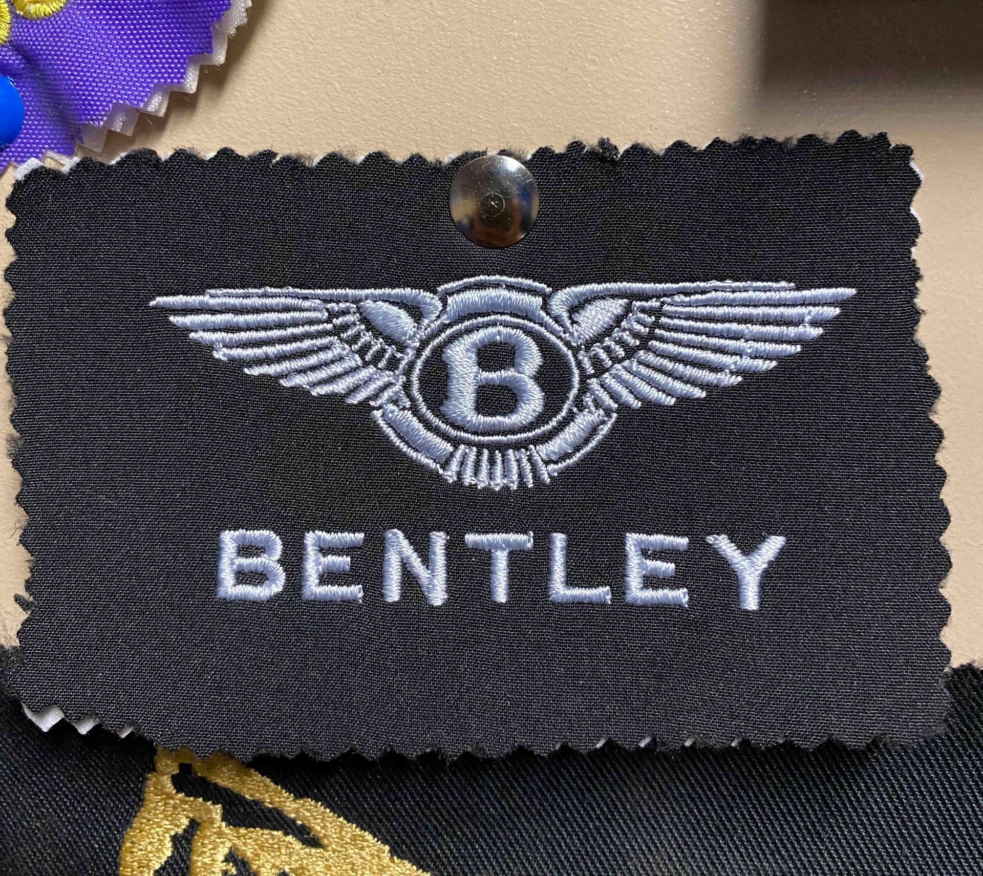Black Bentley embroidery emblem patch with silver wings and lettering, pinned to fabric.