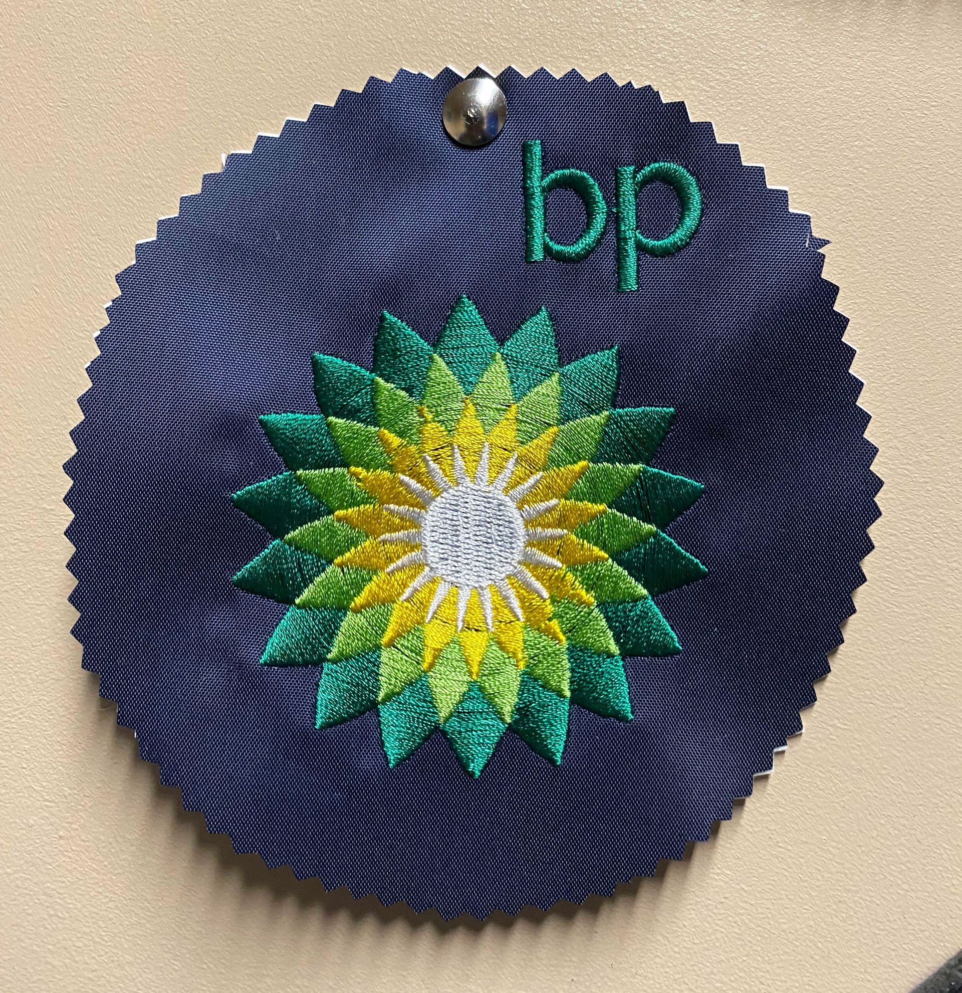 Embroidered BP logo on navy fabric. Features a green, yellow, and white flower design with the letters