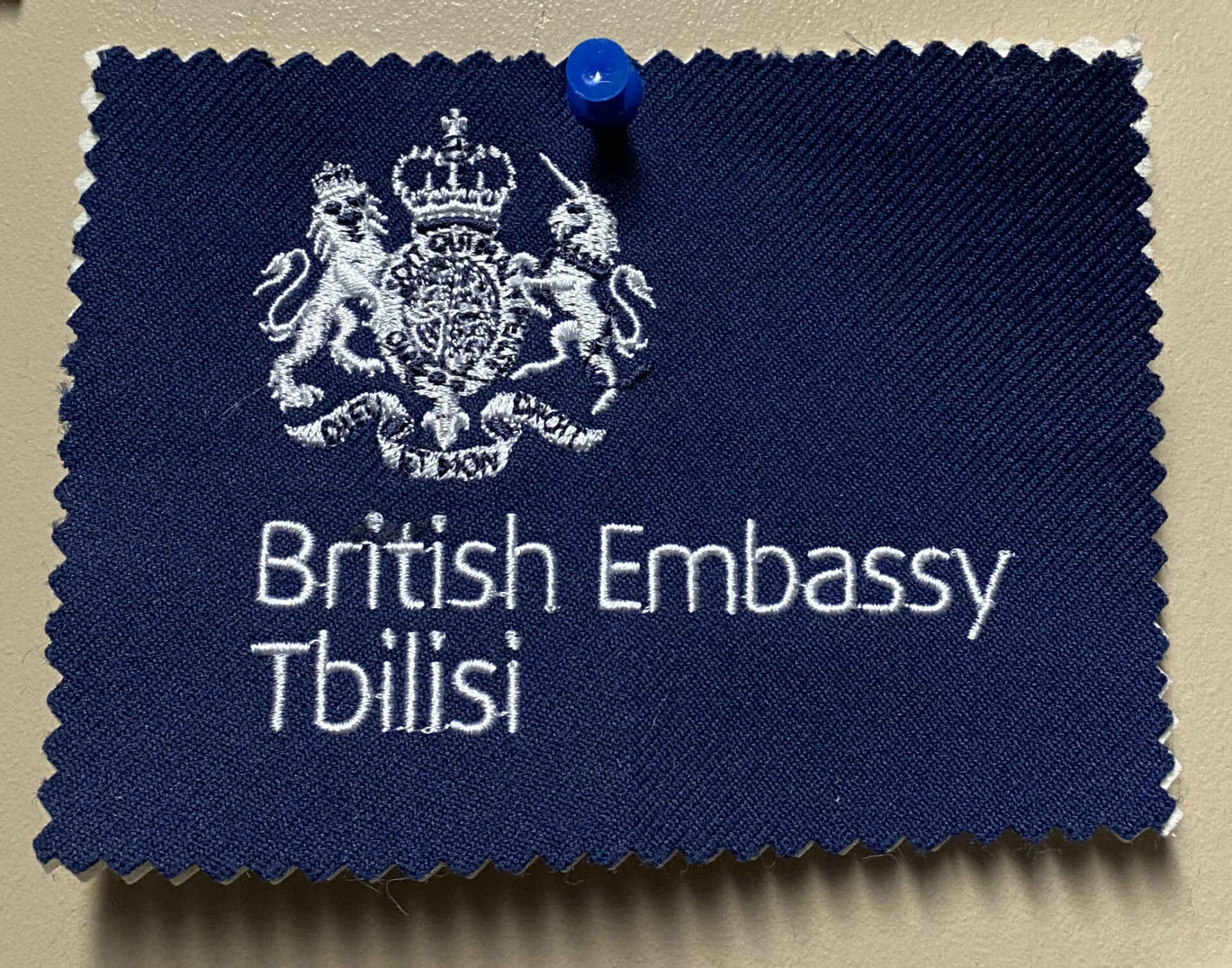A dark blue patch embroidered with the British Embassy Tbilisi emblem, pinned to a beige surface.