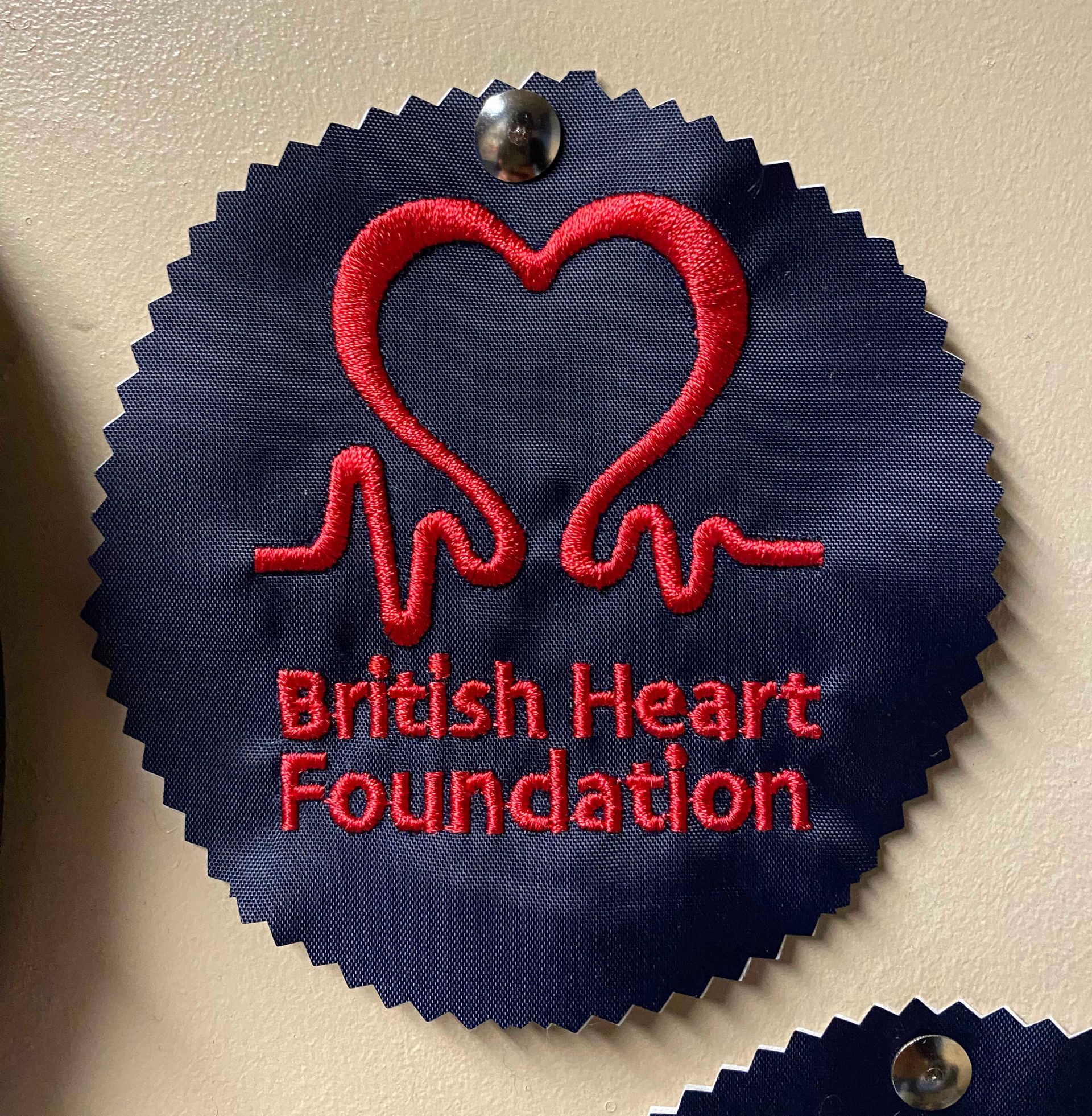 Dark blue ribbon with red embroidered heart and heartbeat line. Text: