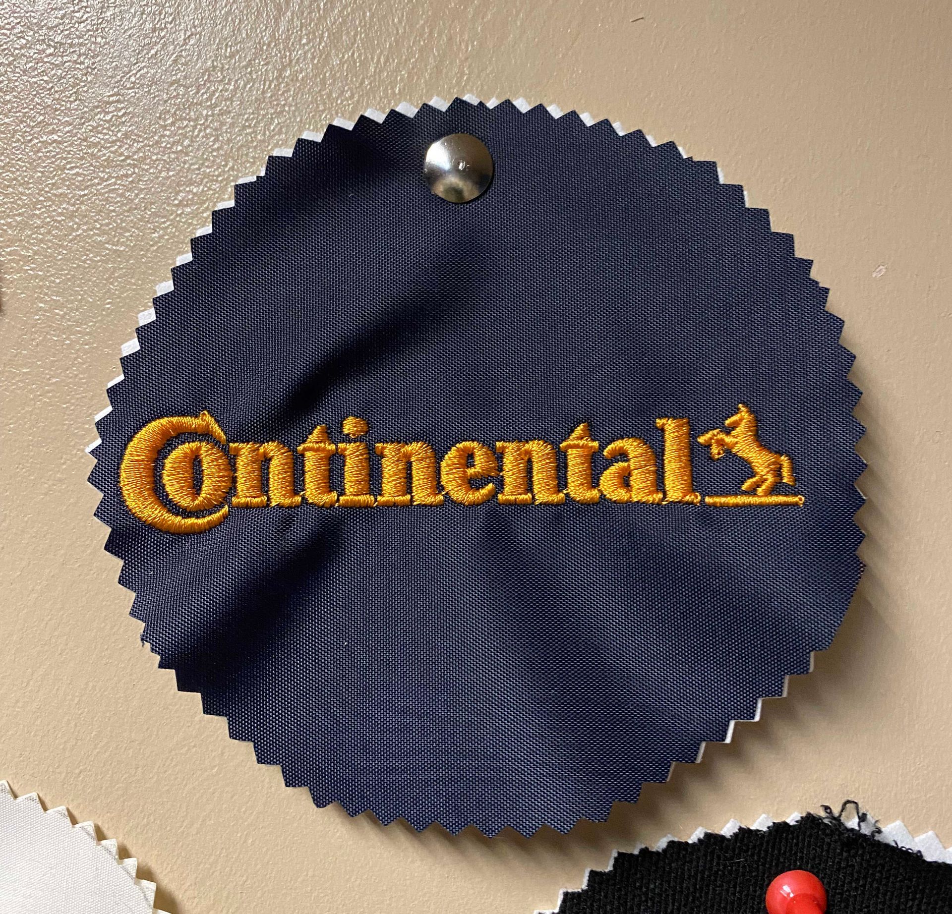 A circular fabric swatch with a blue textured surface. The Continental logo is embroidered in gold.